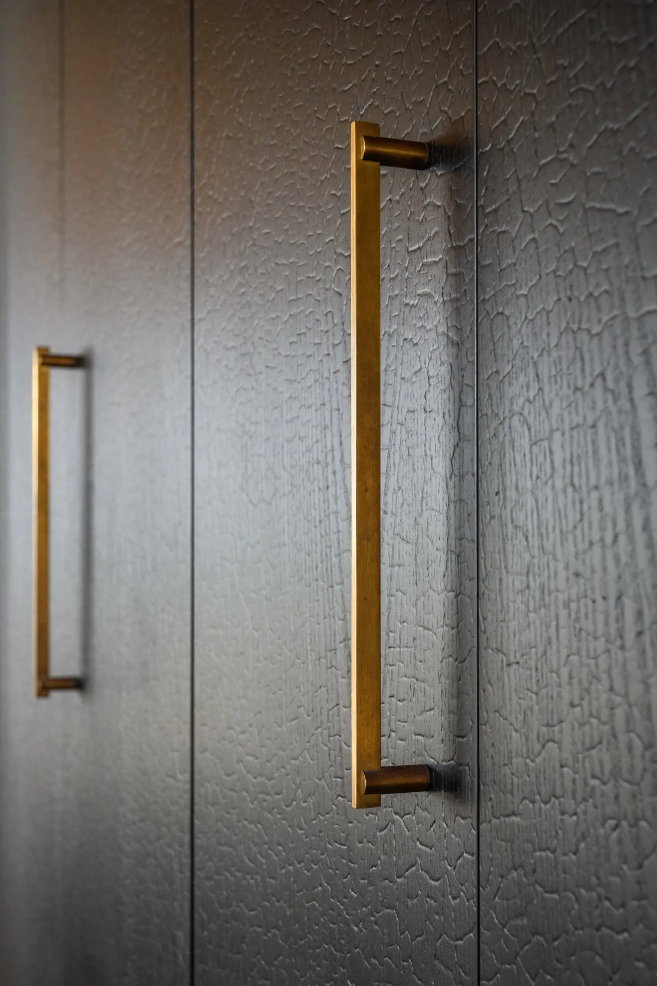Raking light across aged brass pulls on Charred Oak doors