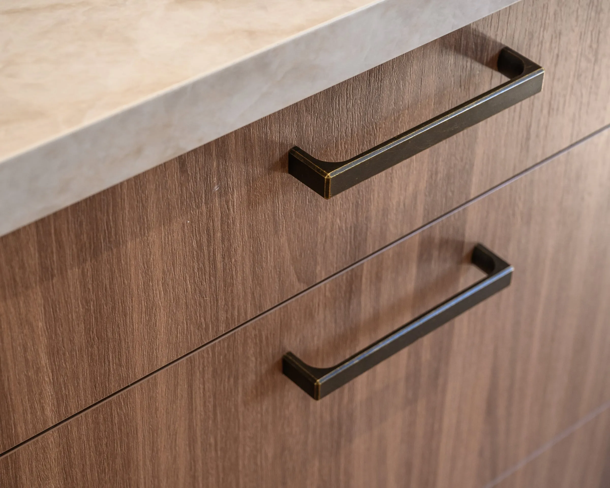 Antique-brass bar pulls on Walnut drawer fronts beneath a stone benchtop edge