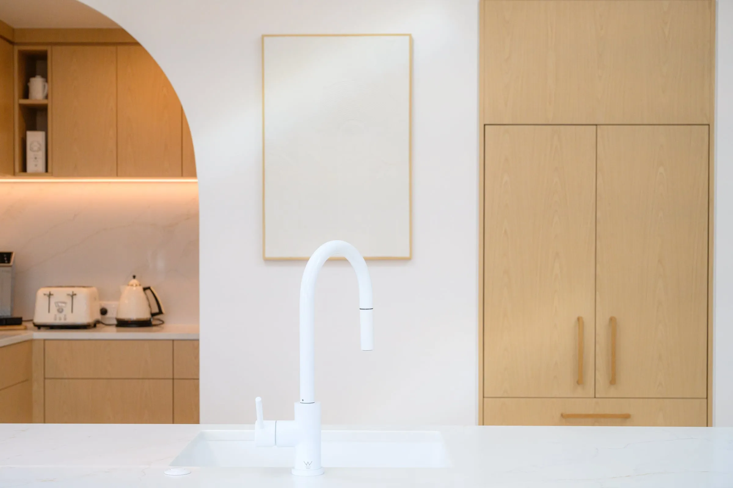Arched scullery opening, integrated fridge and white tap in the foreground