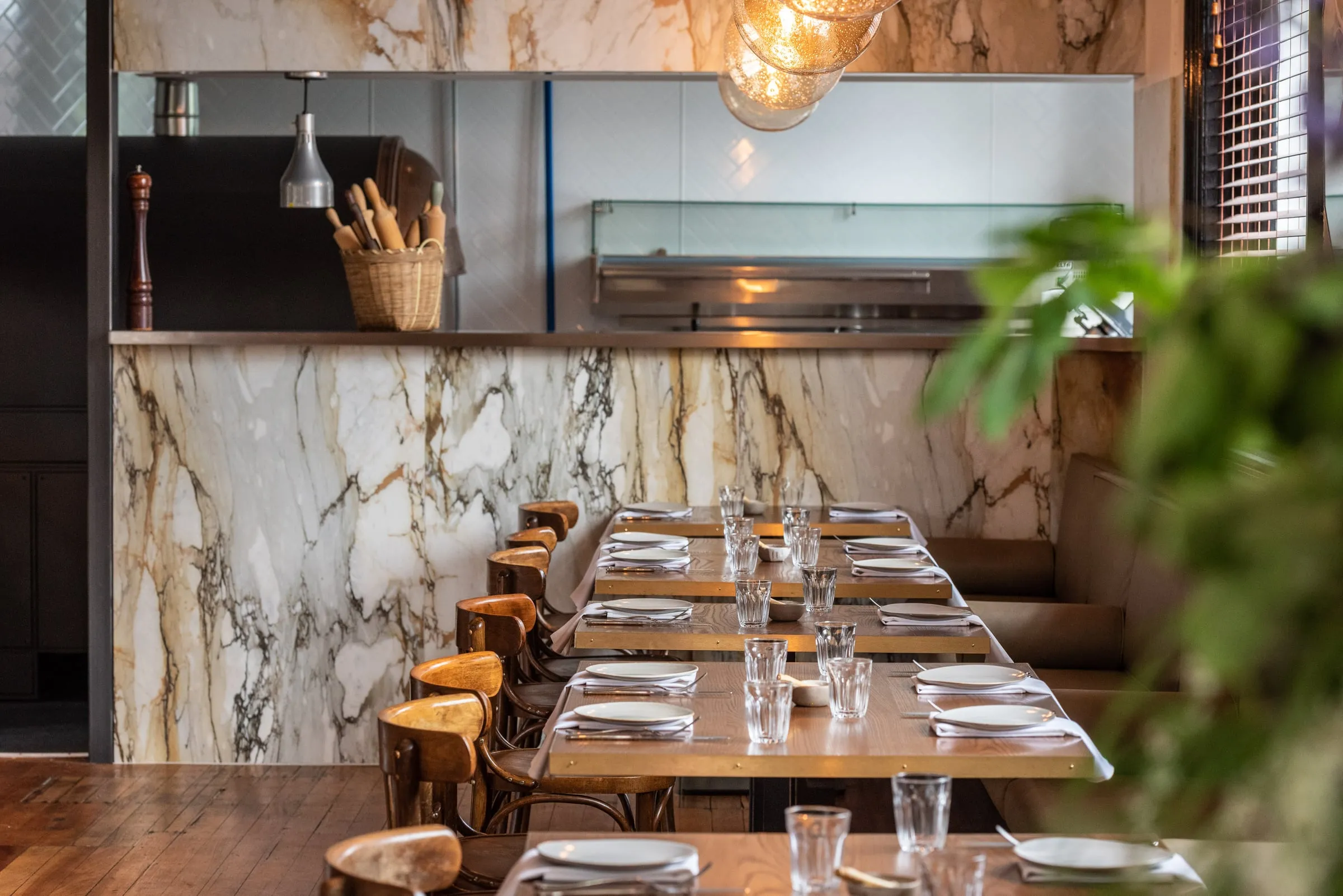 Dining room with brass-edged Oak tables facing a Marble-clad open kitchen pass