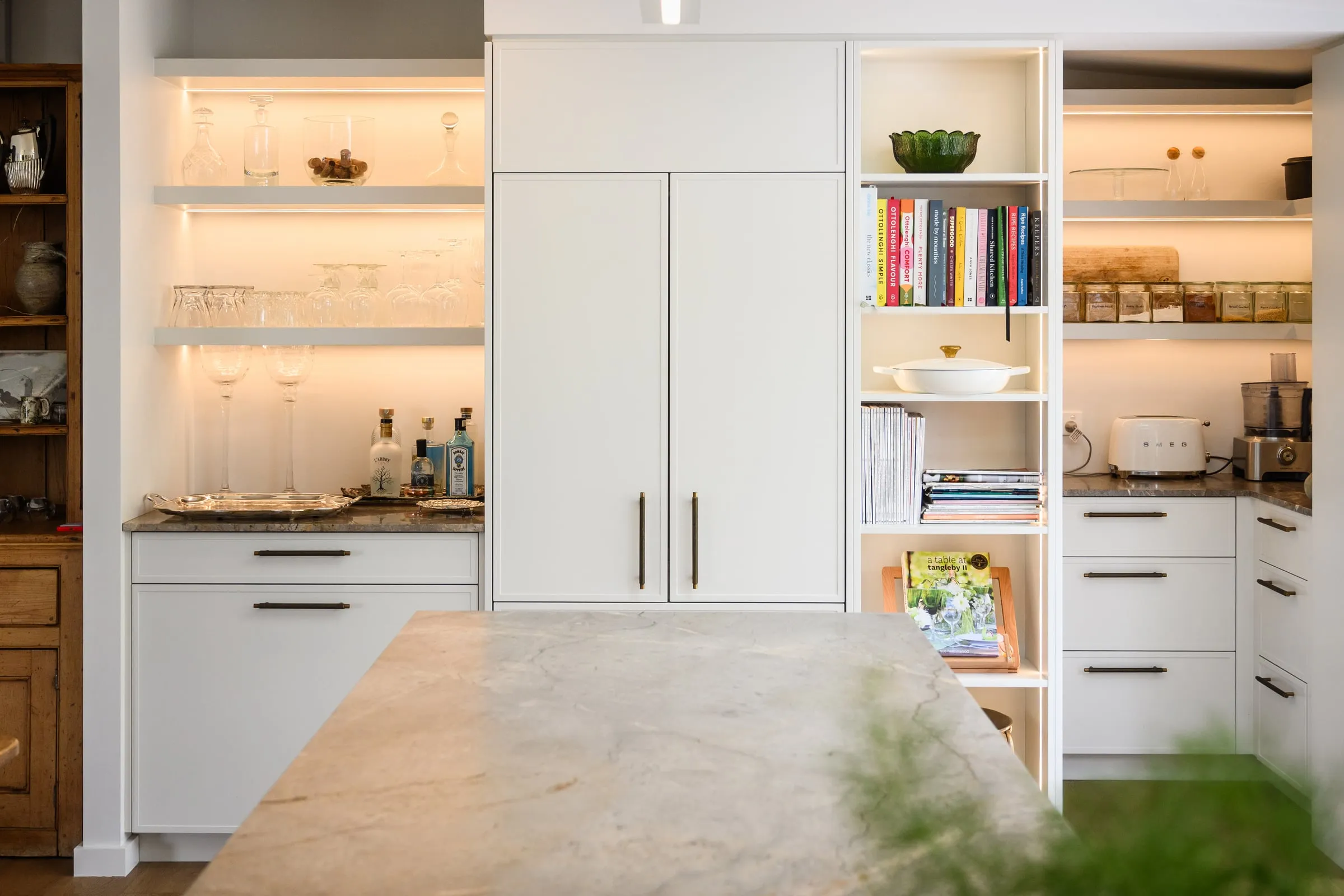 Bar and pantry wall with integrated fridge and warm-lit open shelving