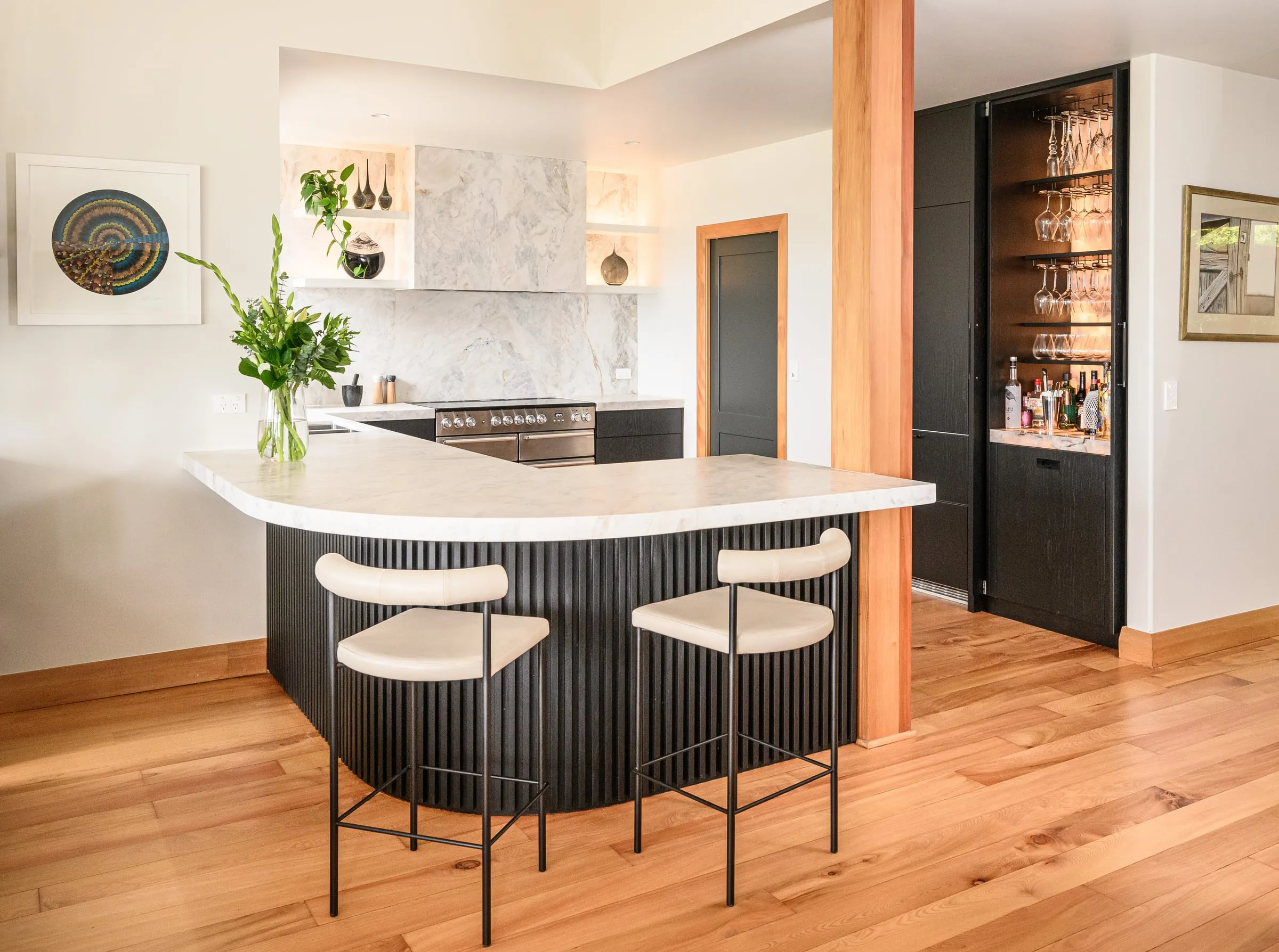 Curved fluted black Oak island with cream bar stools and timber post