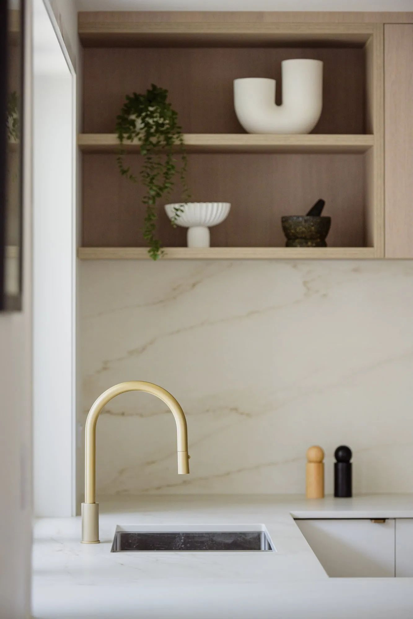 Brushed-brass gooseneck tap over undermount sink and veined splashback