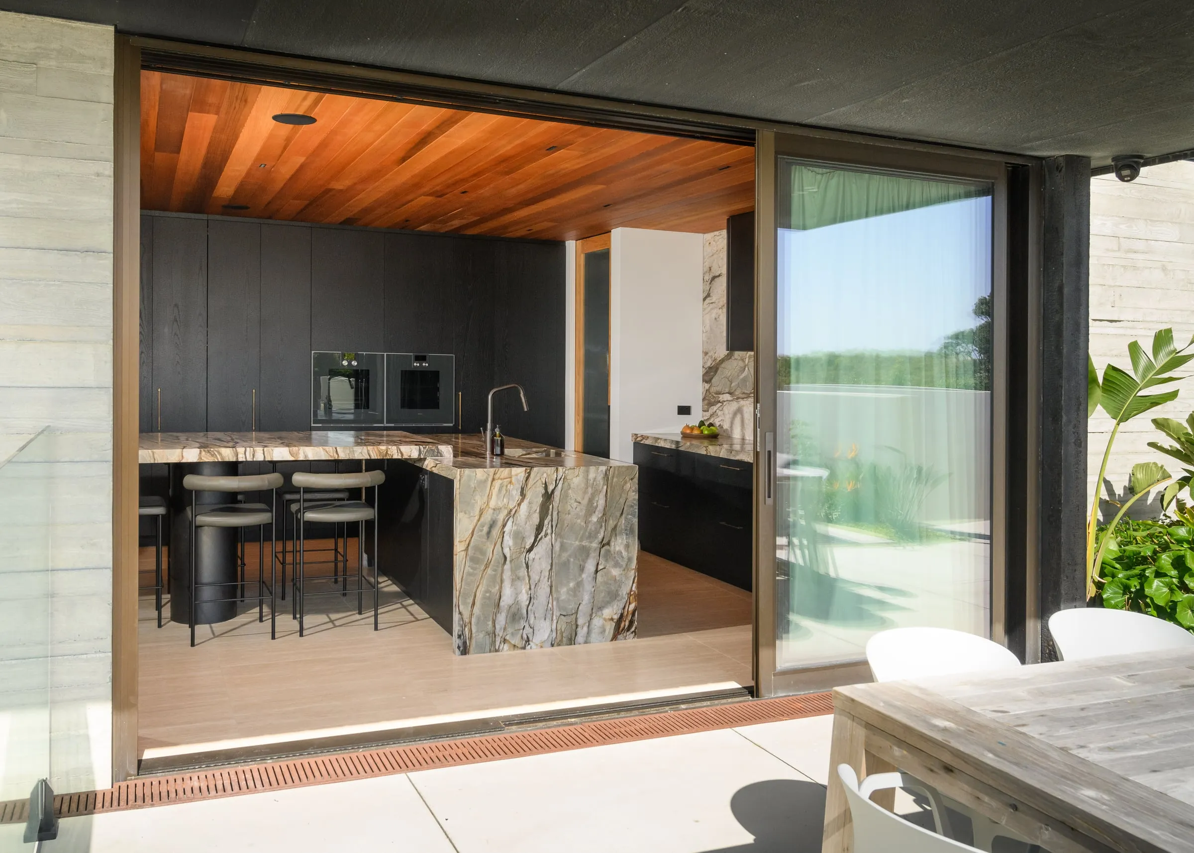 Coastal kitchen seen through open sliders from a concrete terrace