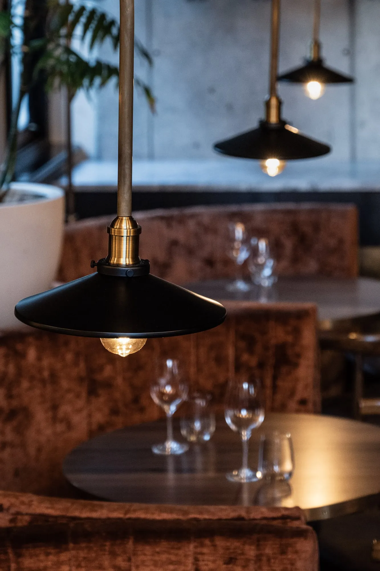 Black and brass pendants in sharp focus above rust velvet booths