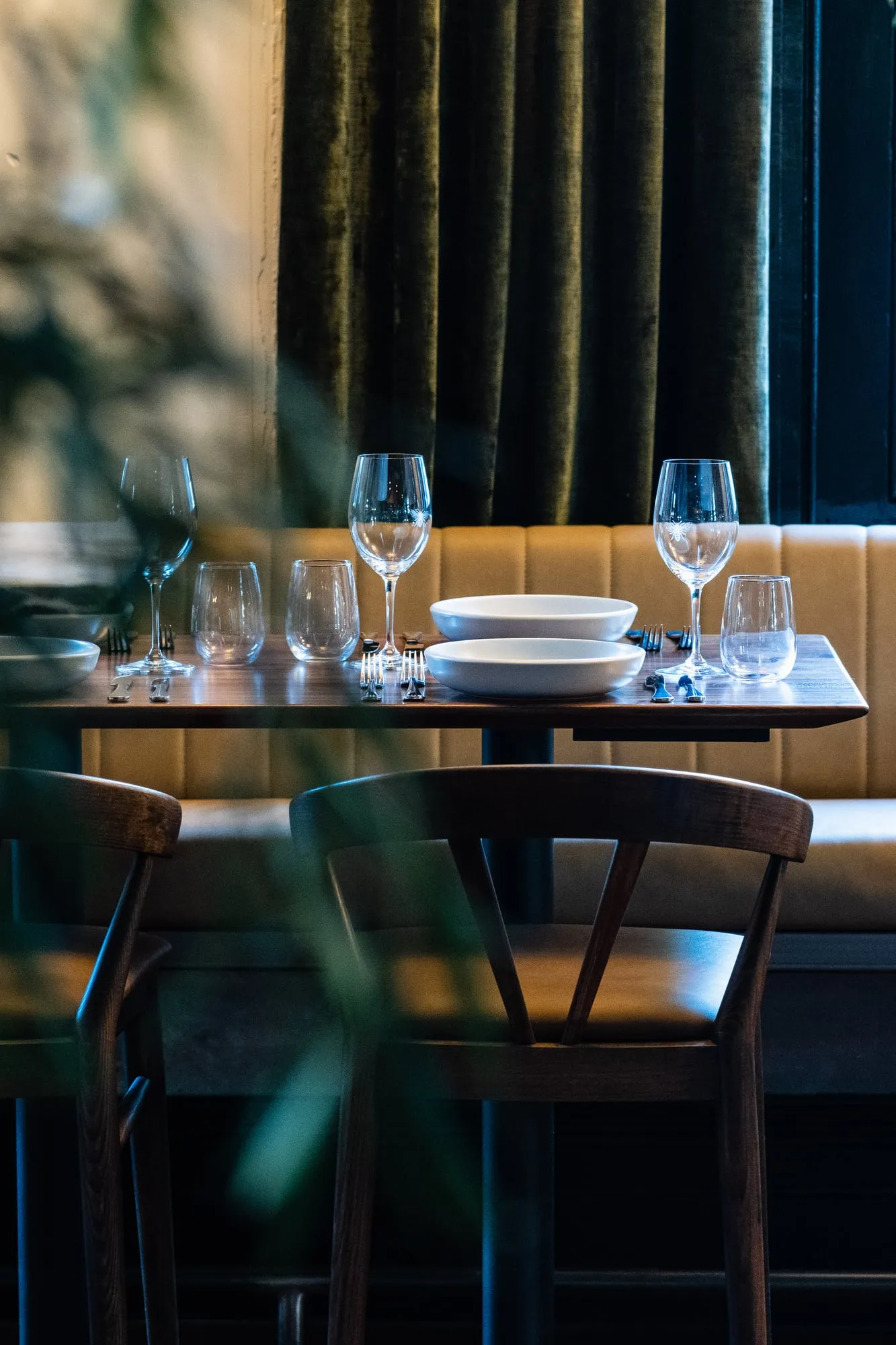 Corner banquette table with olive velvet curtain seen through soft foliage
