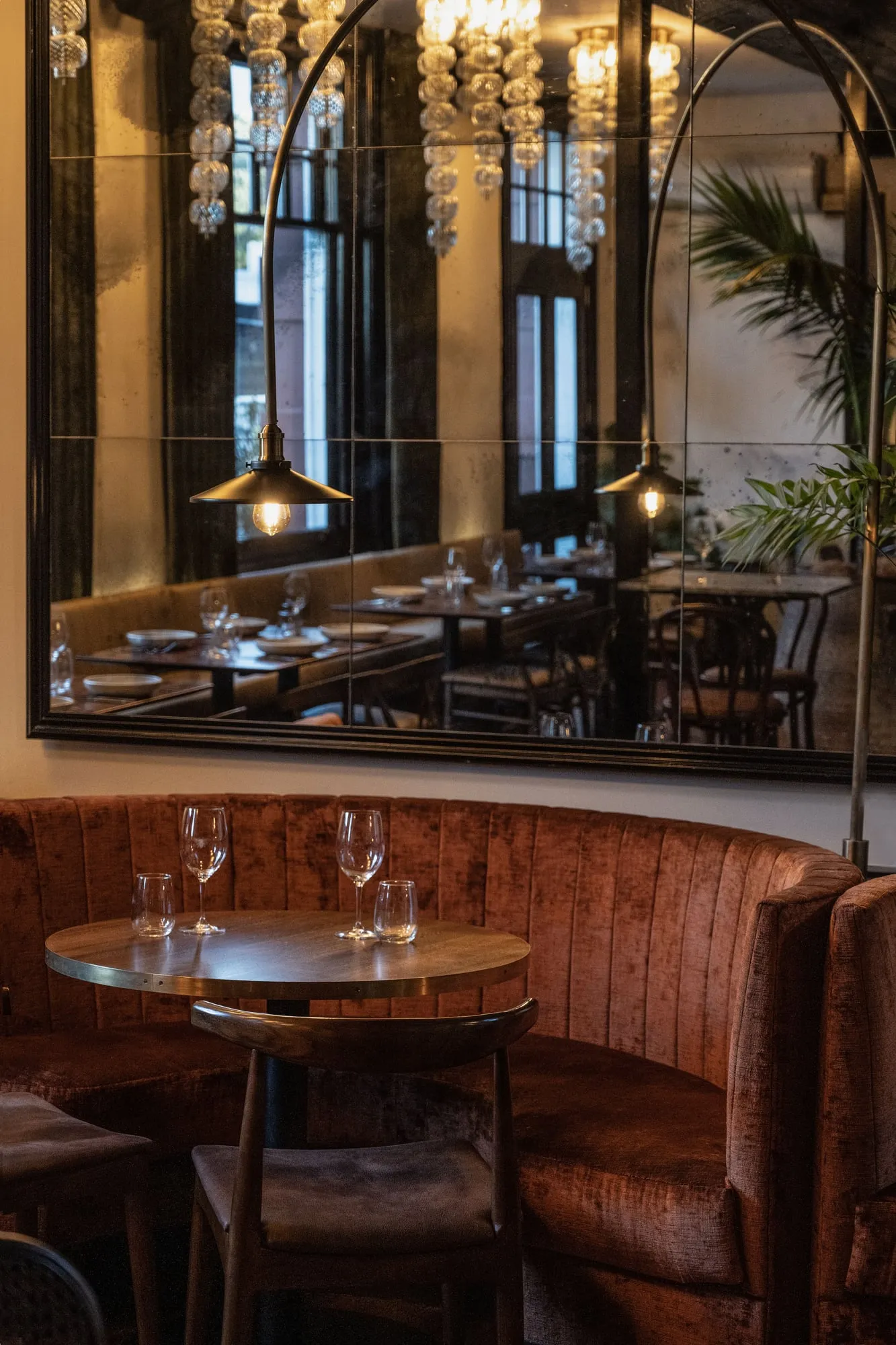 Curved rust velvet banquette with brass-edged round table and antiqued mirror