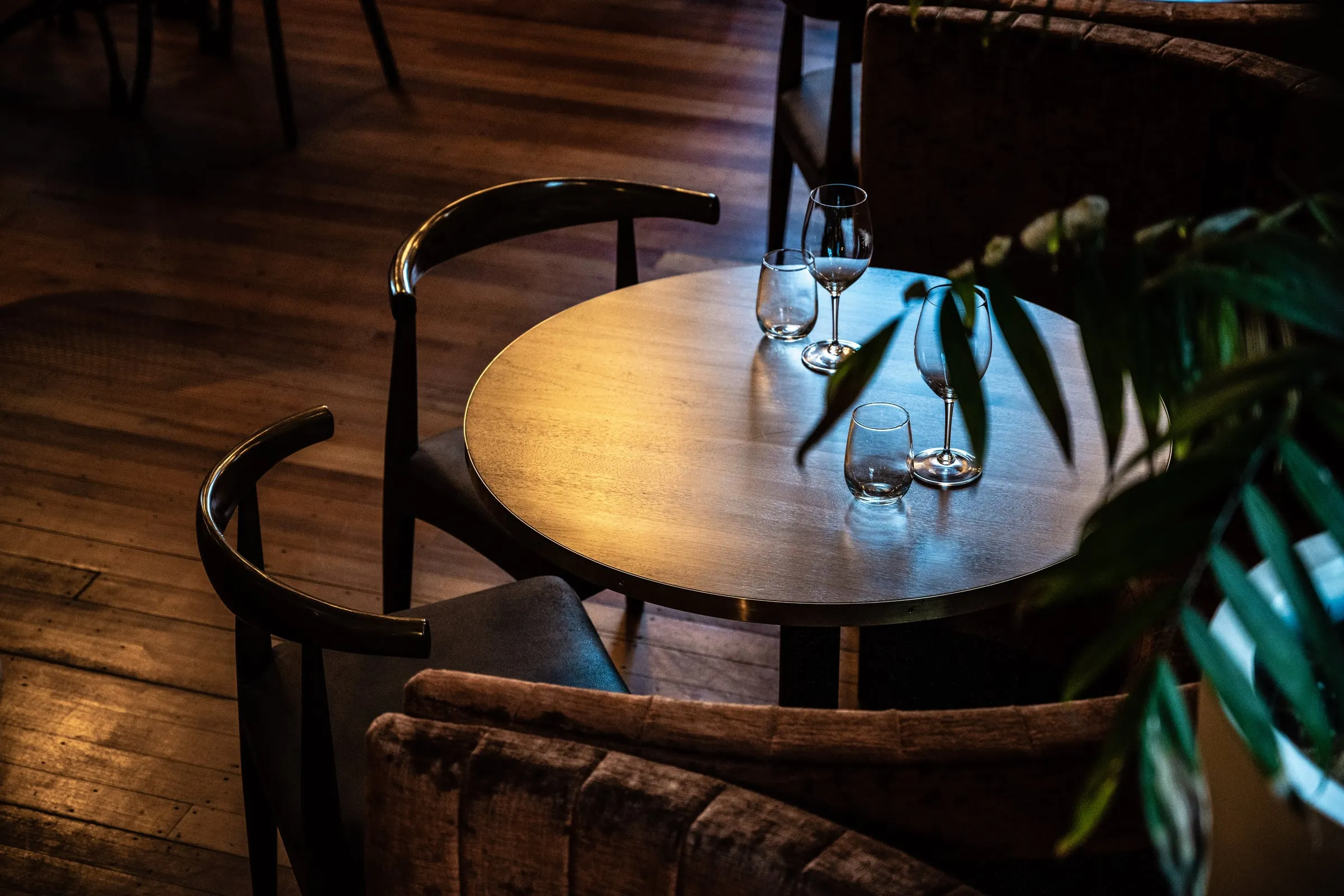 Round table with elbow chairs and velvet tub seats lit for evening service