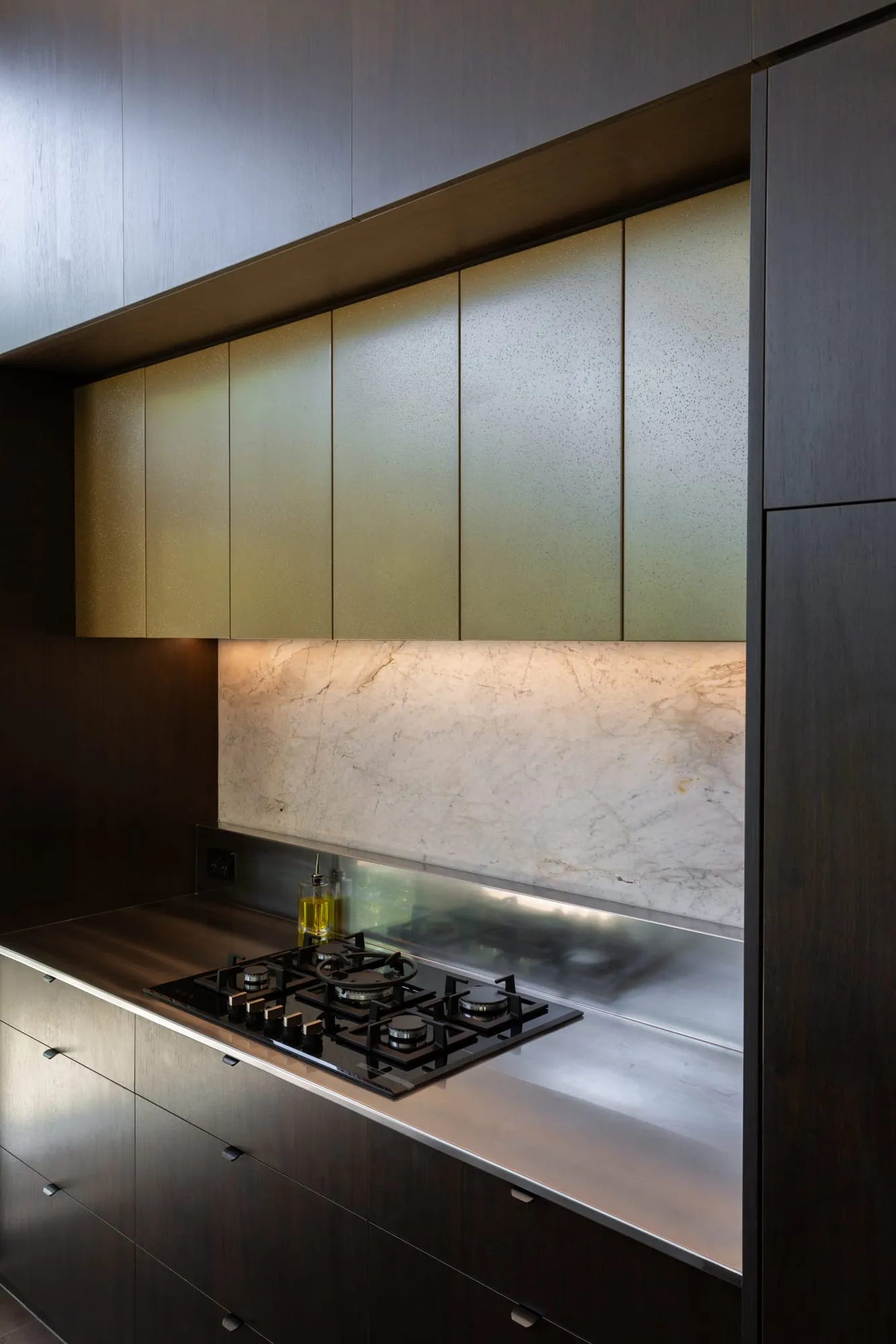 Champagne-brass upper doors over the lit Quartzite splashback and gas hob