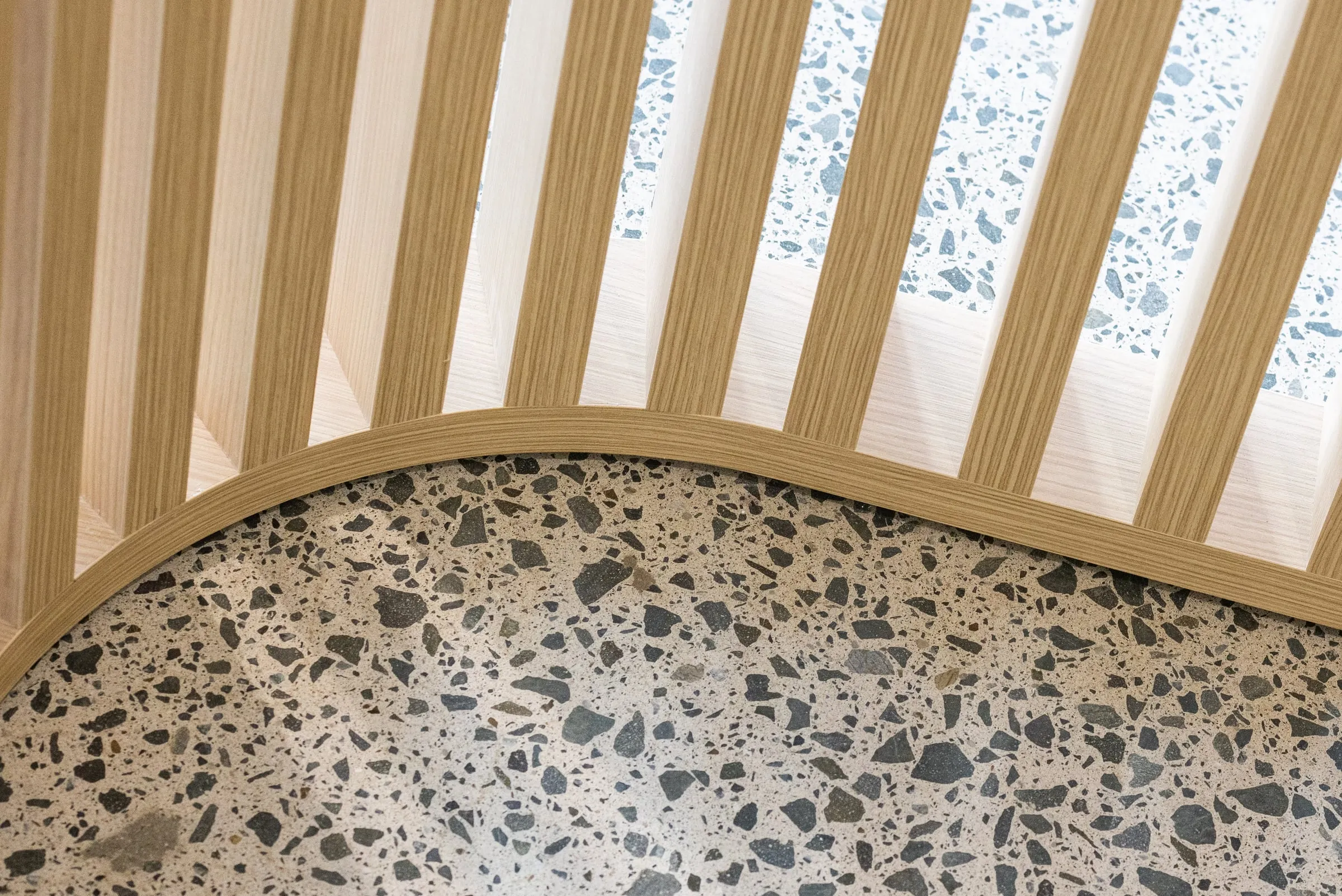 Curved Ash batten base rail meeting salt-and-pepper terrazzo floor