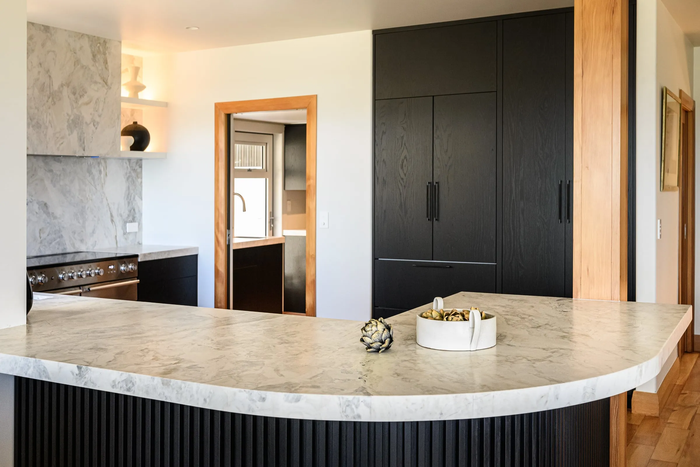 View across the curved stone benchtop into the black Oak kitchen