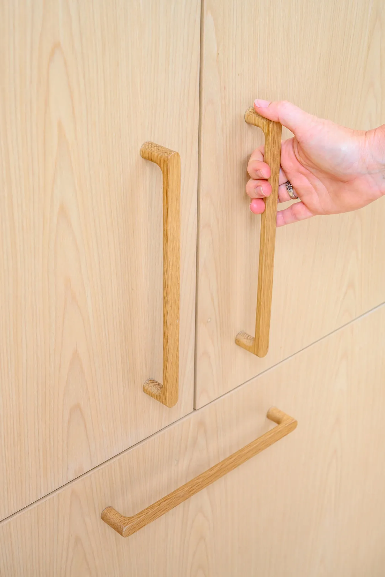 Hand on a custom solid Oak door pull, grain legible