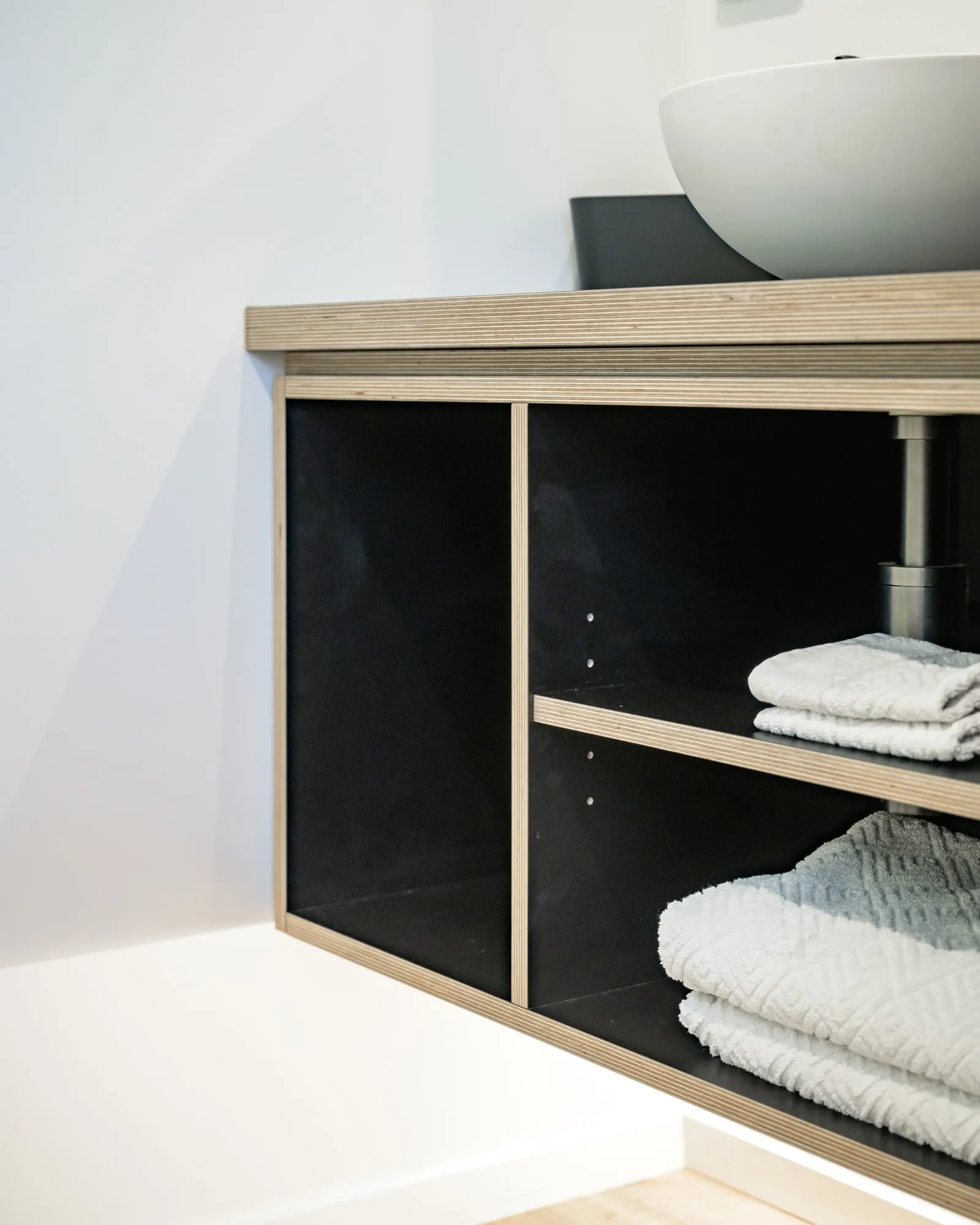 Exposed Birch plywood edge on a floating vanity against black panels