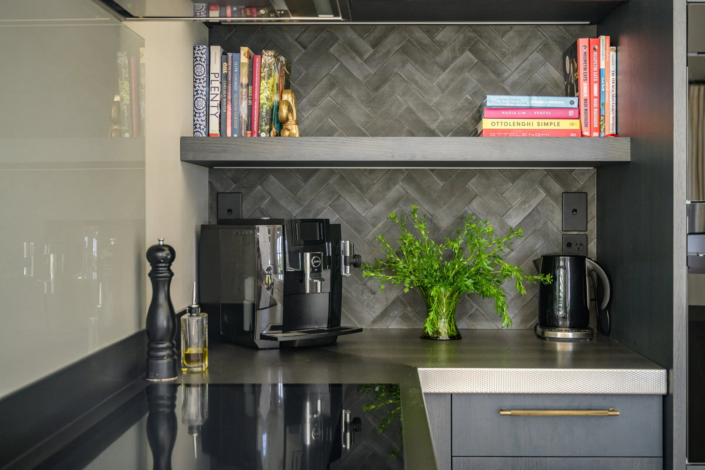 Floating Oak shelf with cookbooks above a herringbone tile splashback