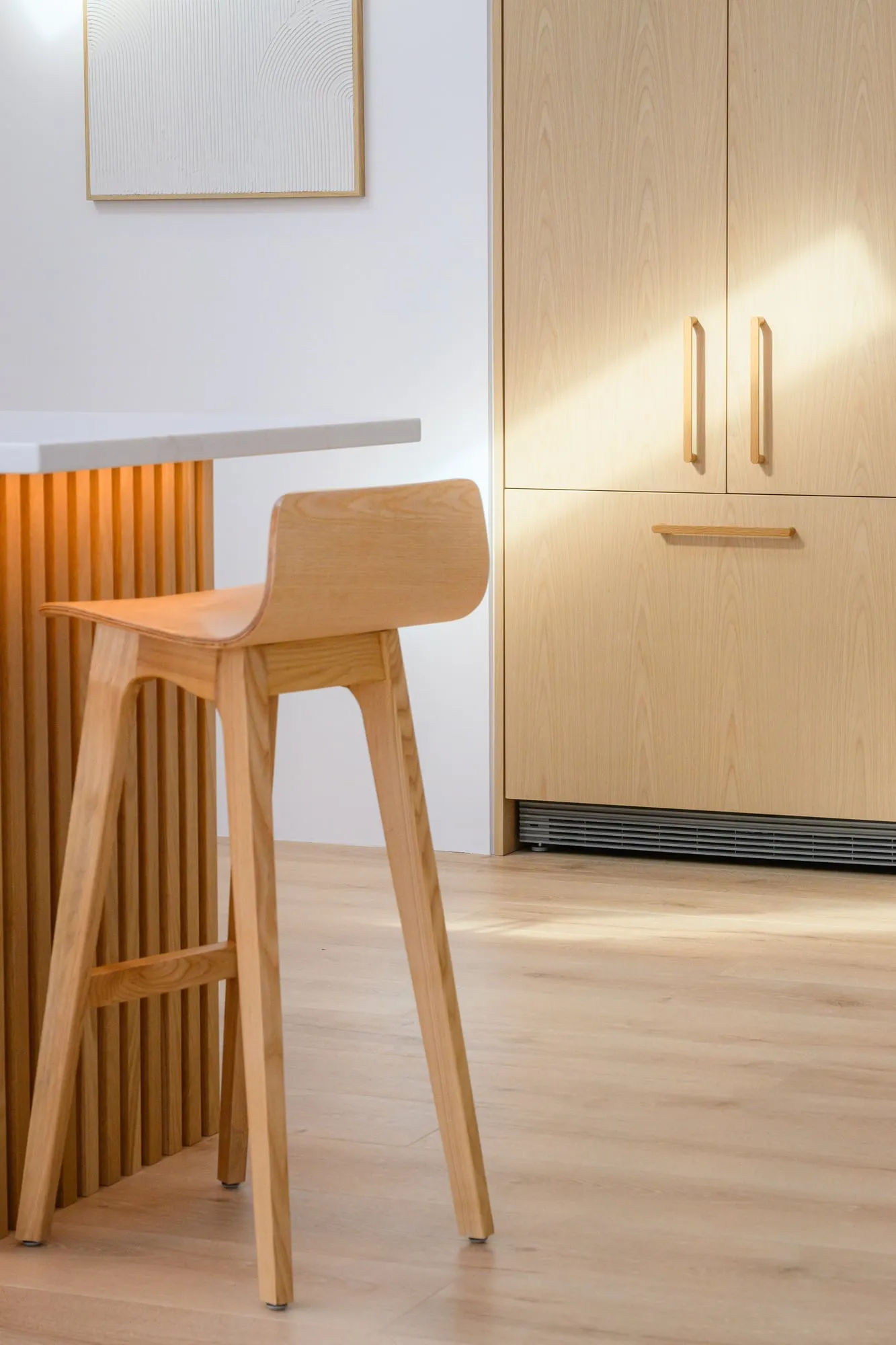 Fluted island edge and Ash barstool, afternoon light raking the tall cabinet