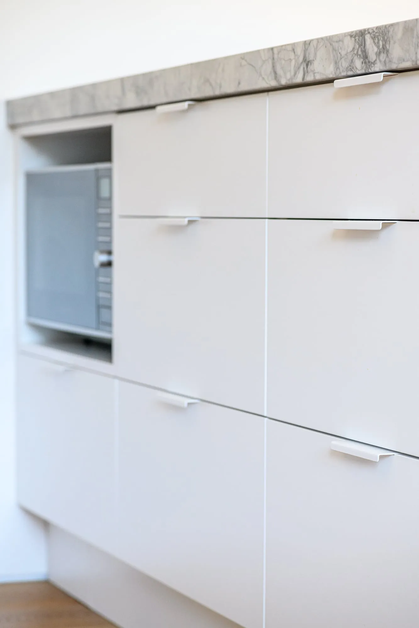 White drawer fronts with folded edge pulls beneath the stone overhang