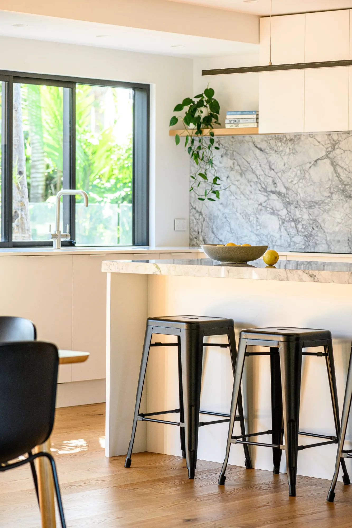 Black-framed window with garden greenery, stone panel and stools