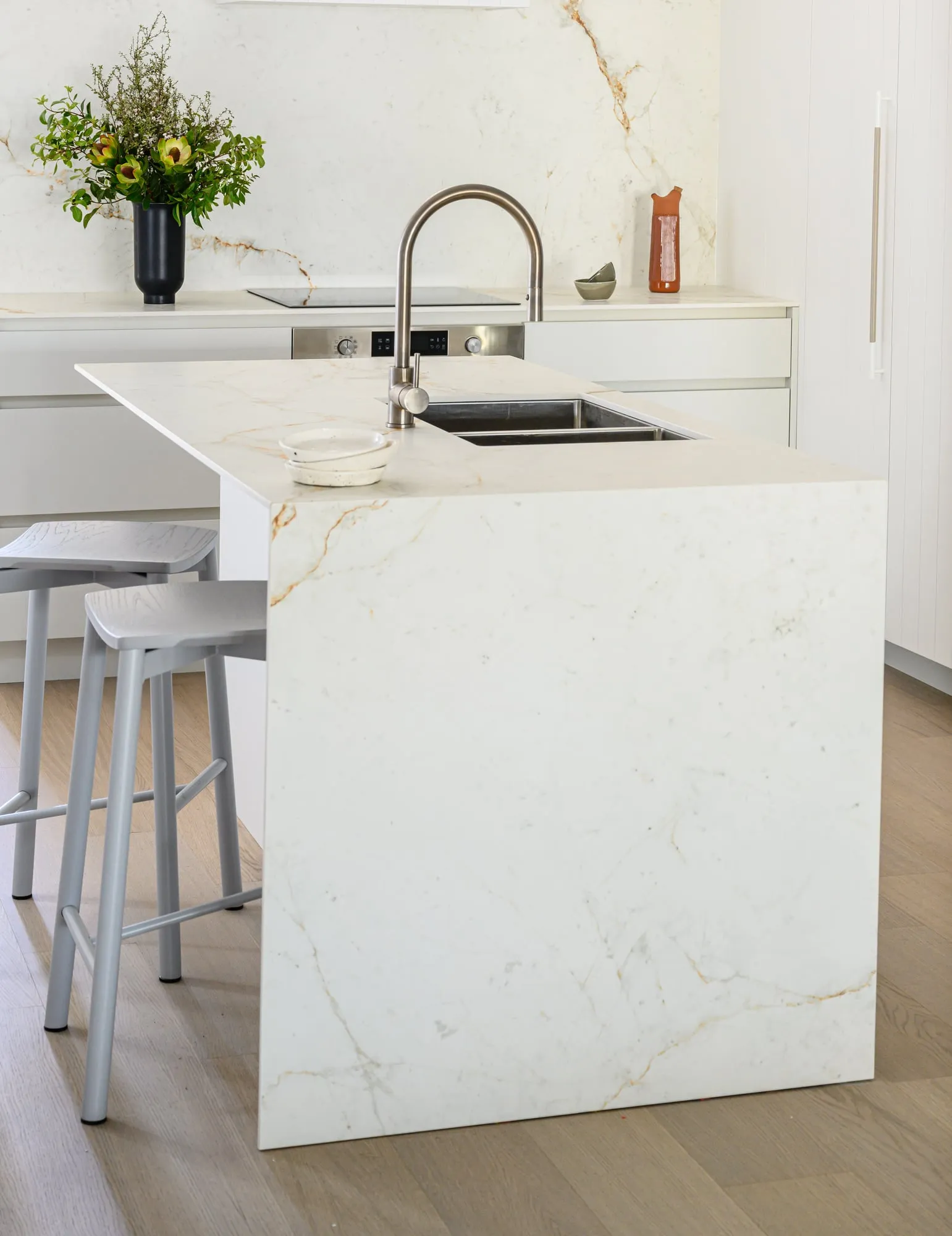Showroom kitchen display with gold-veined stone waterfall island in daylight