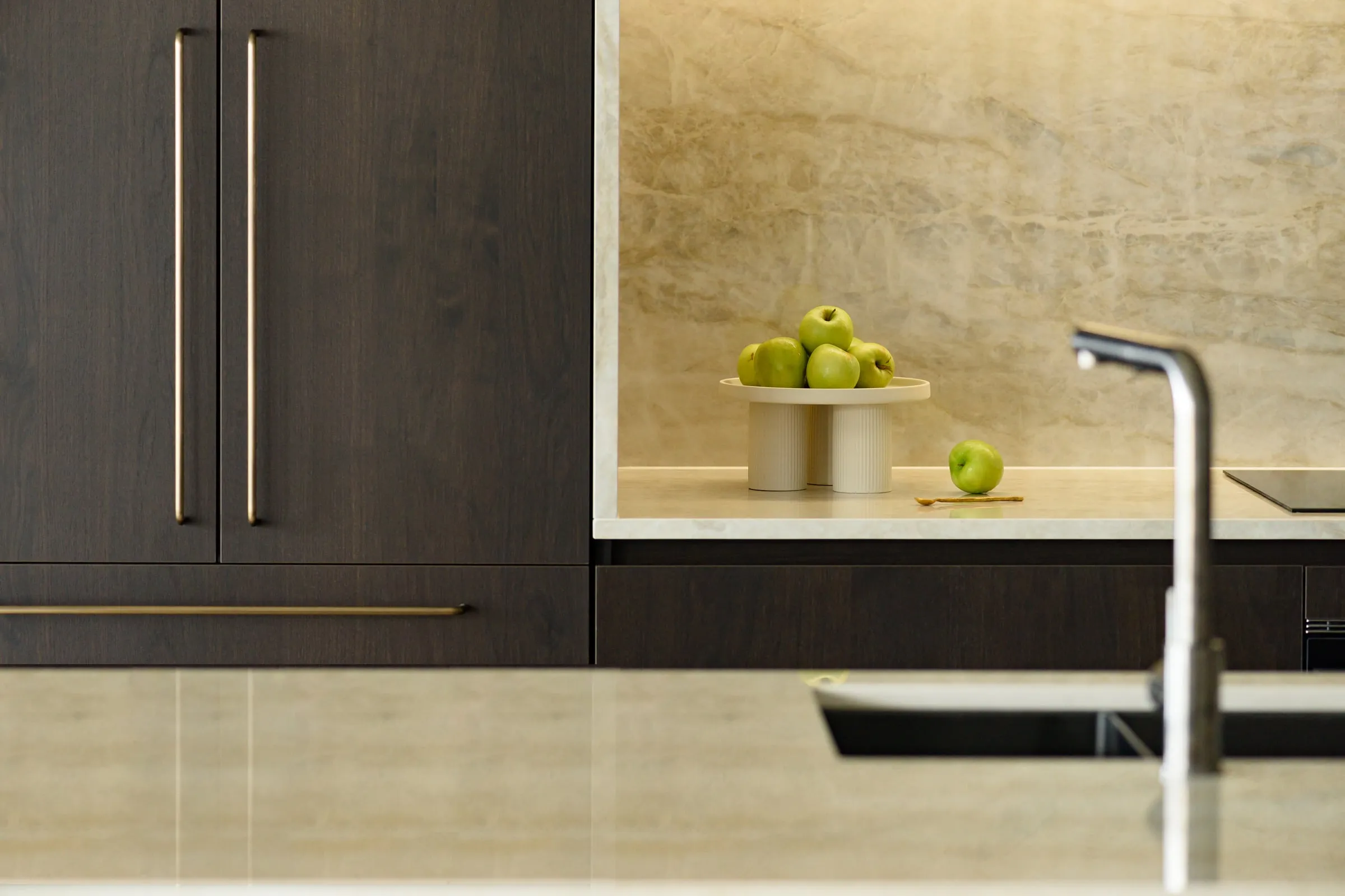 Dark smoked walnut showroom cabinetry with brass pulls and lit stone niche