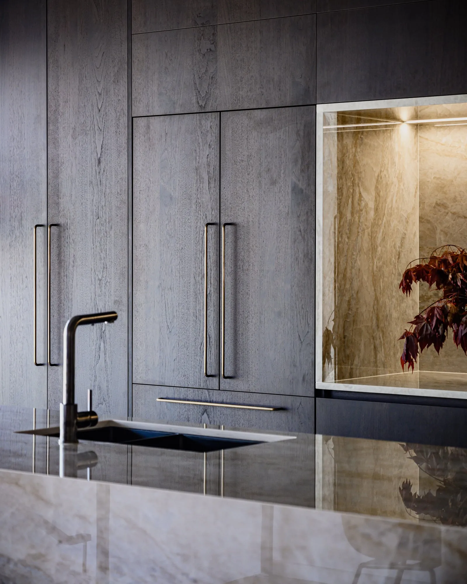 Smoked walnut cabinetry with twin brass pulls and a glowing stone niche