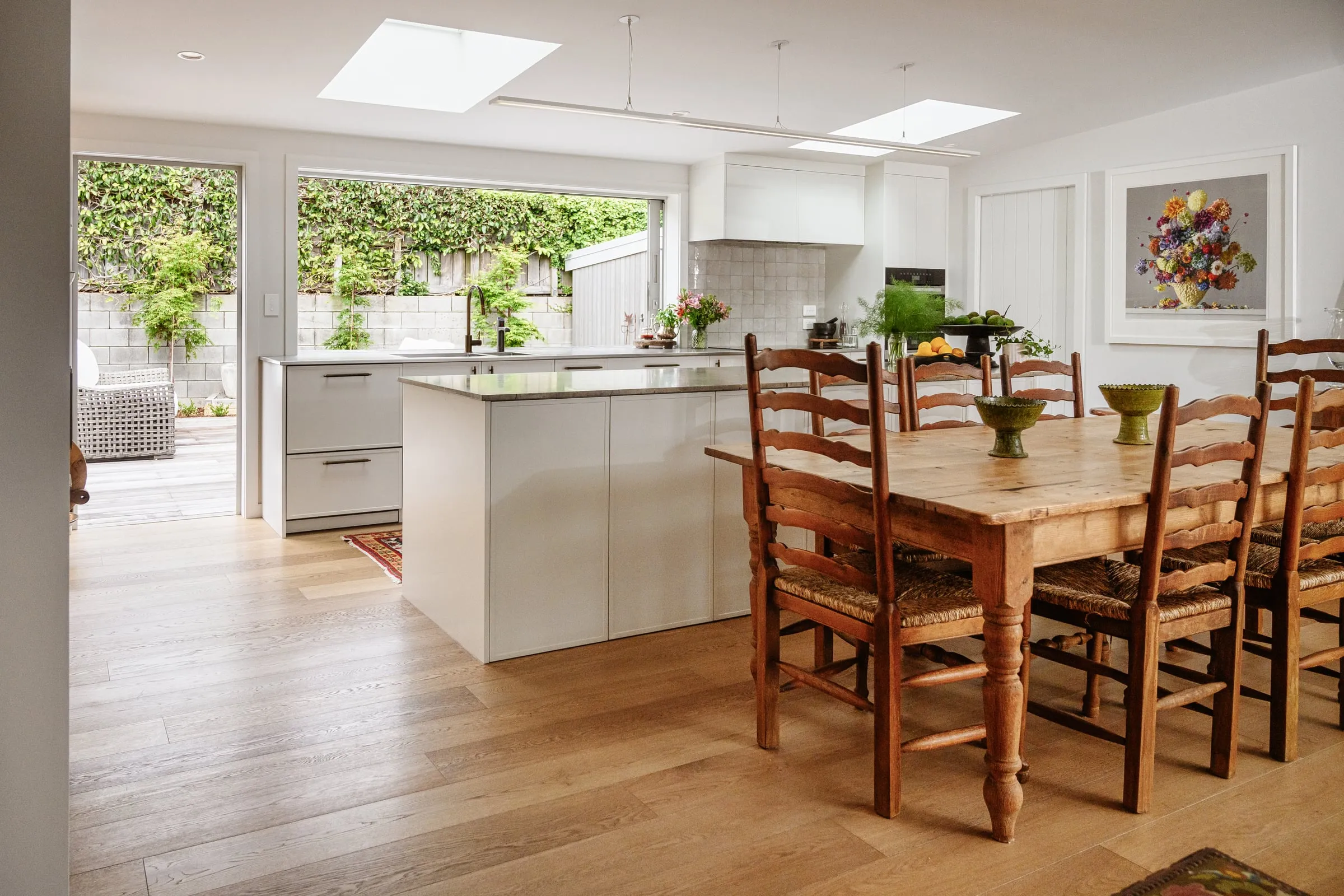Open-plan ivory shaker kitchen and farmhouse dining table under skylights