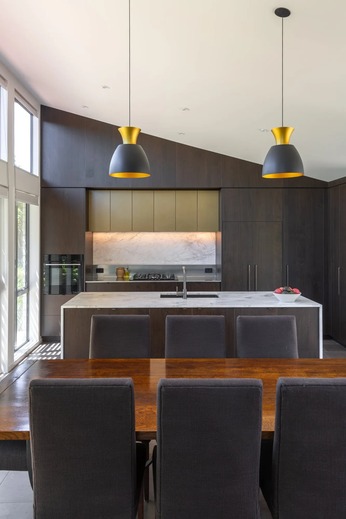 Kitchen and dining under a raked white ceiling with black and gold pendants