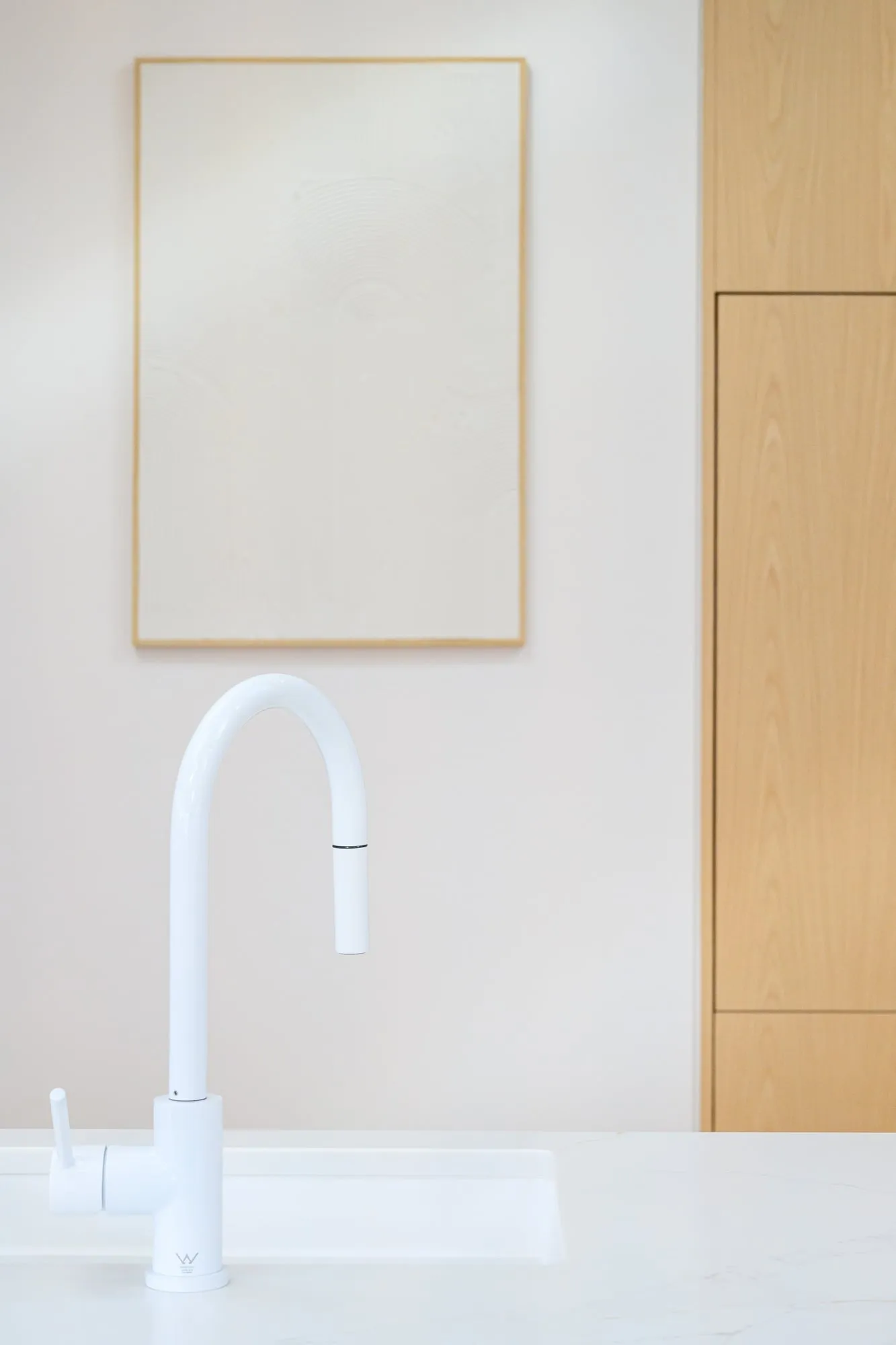 Matte white gooseneck tap against blush wall and timber cabinet