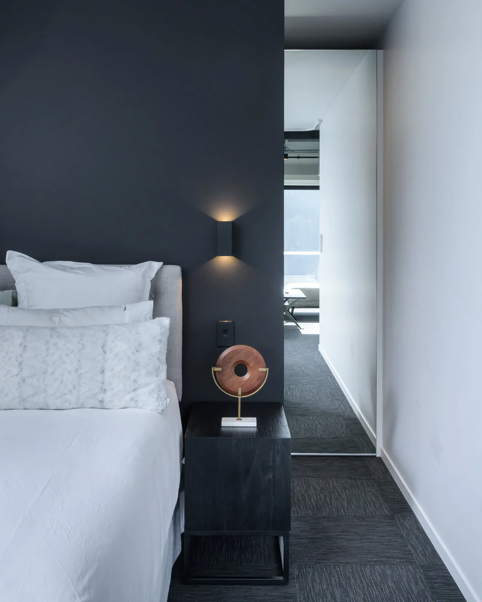 Near-black bedroom feature wall with a single sconce glowing