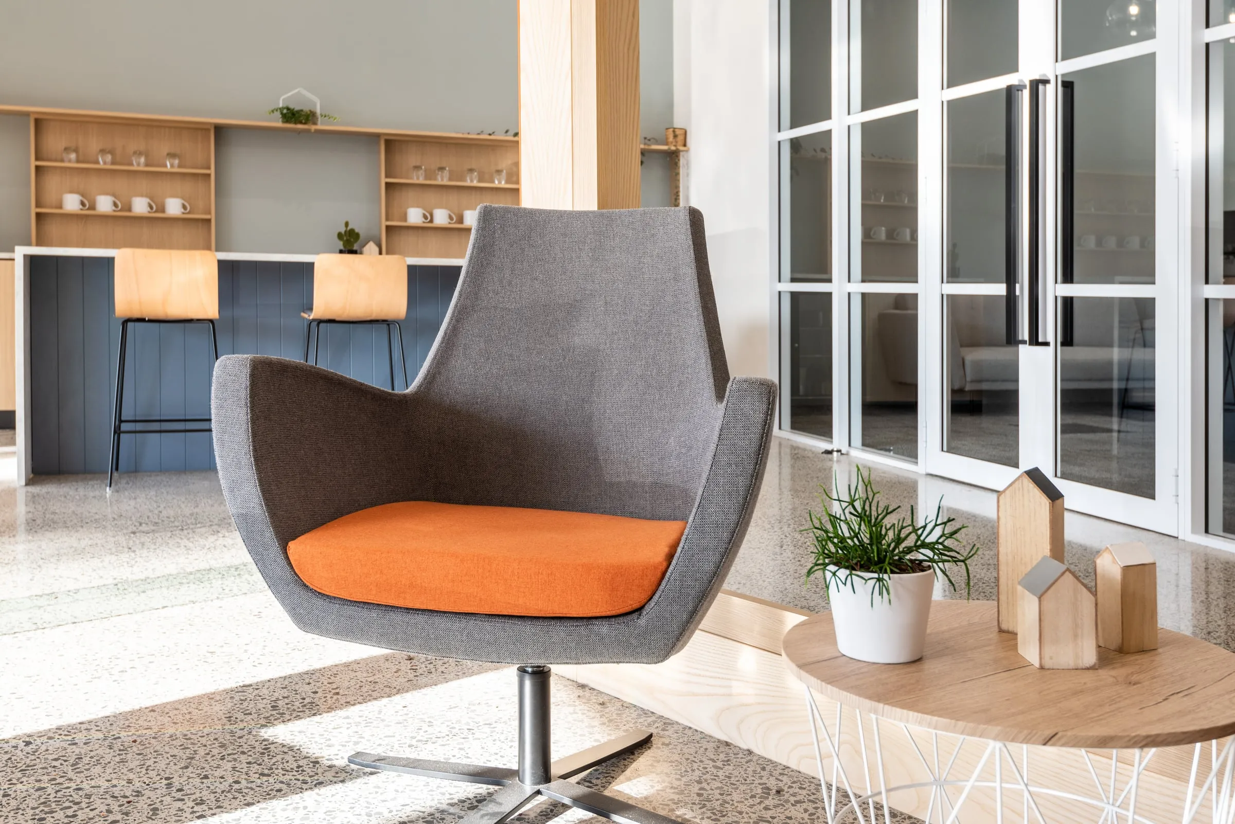 Reception lounge with grey swivel chair, orange seat pad and kitchenette behind