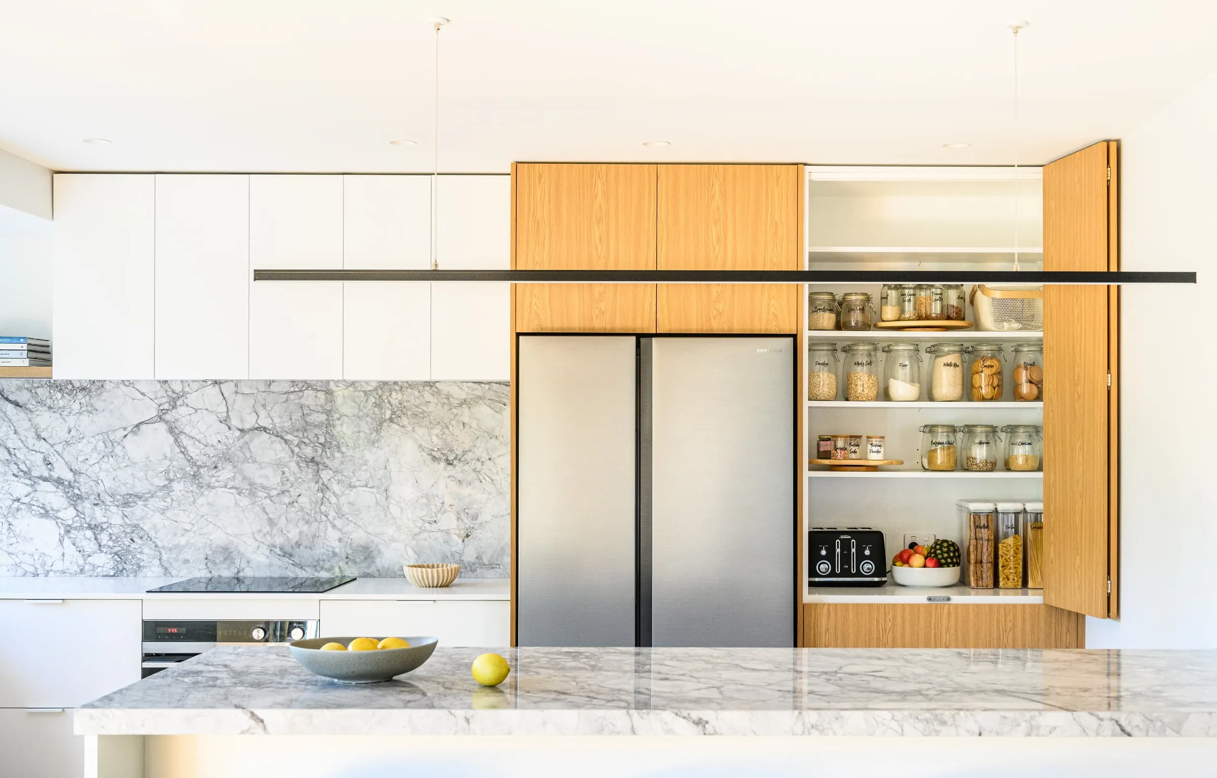 Bi-fold Oak pantry doors open, revealing shelving beside the fridge