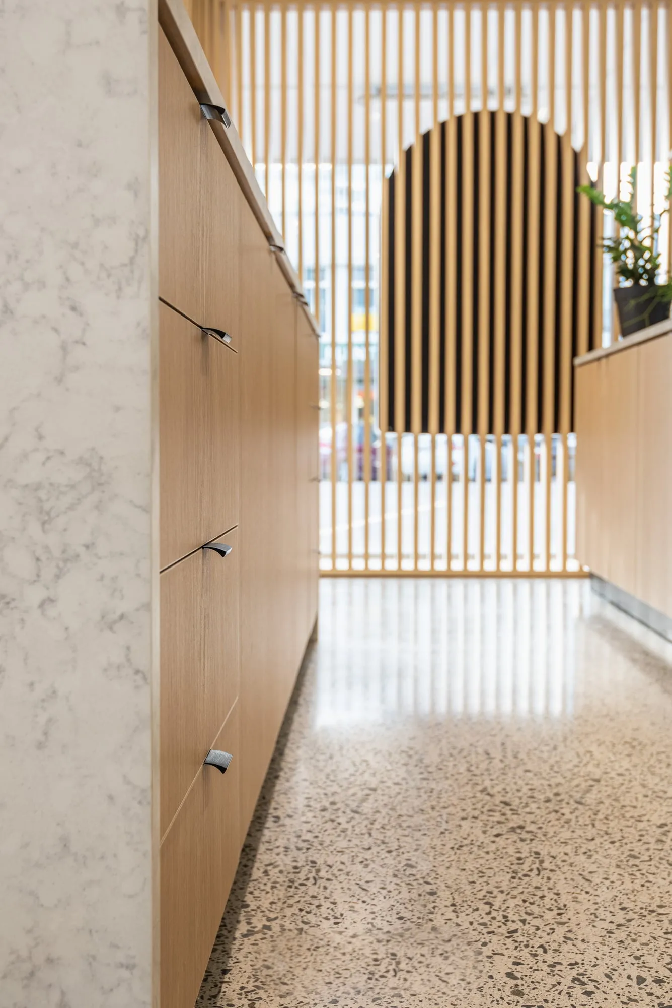 Oak cabinetry run with black tab pulls leading to arched batten screen
