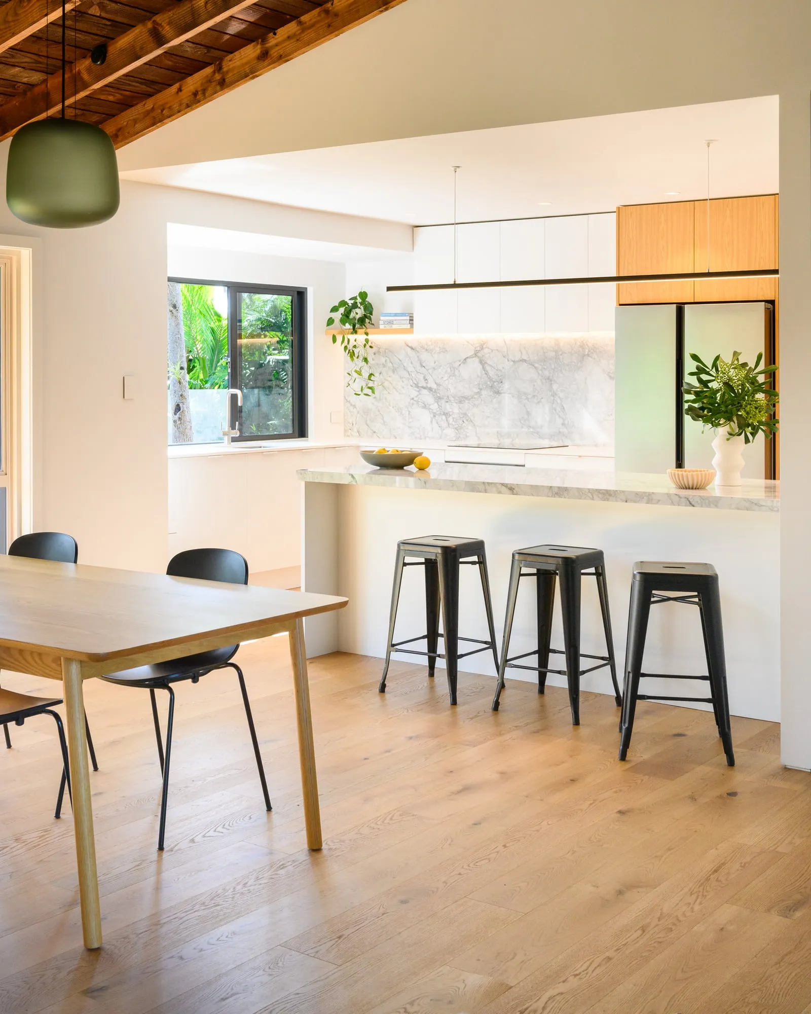 Oak dining table under exposed timber beams and olive pendant
