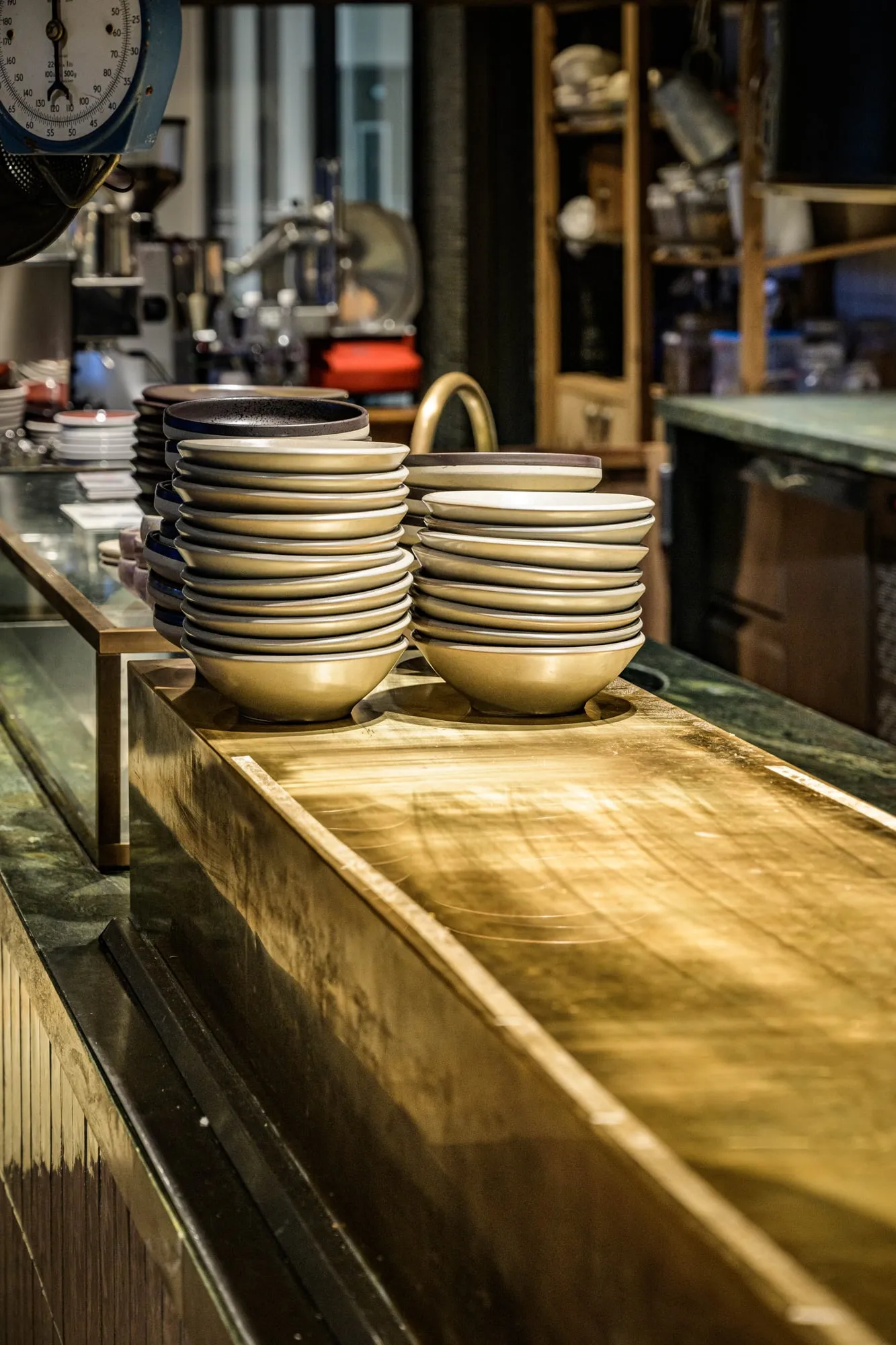 Raking light across an aged brass counter under stacked stoneware bowls