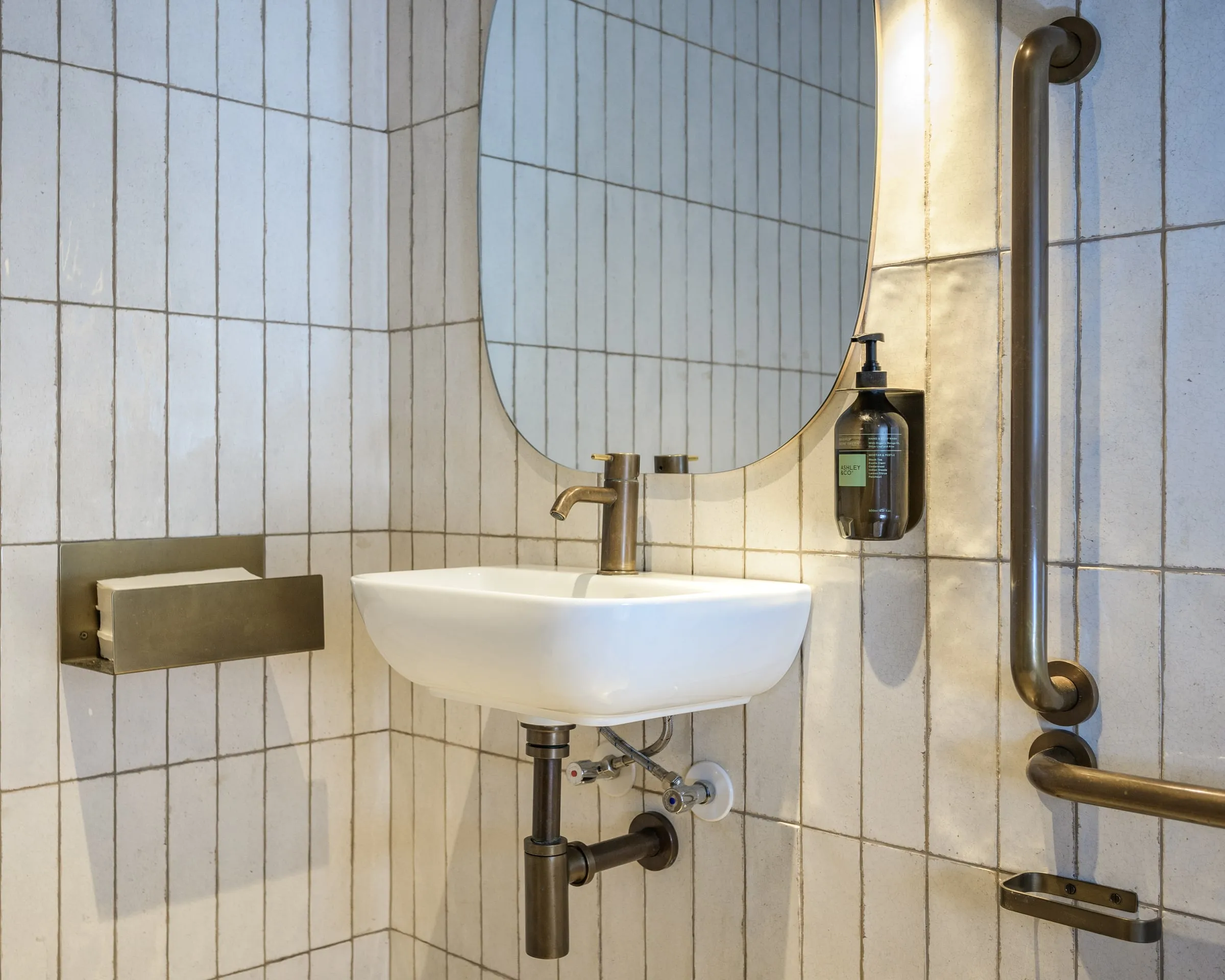 Antique-brass tapware and towel rail against cream stacked-bond tile