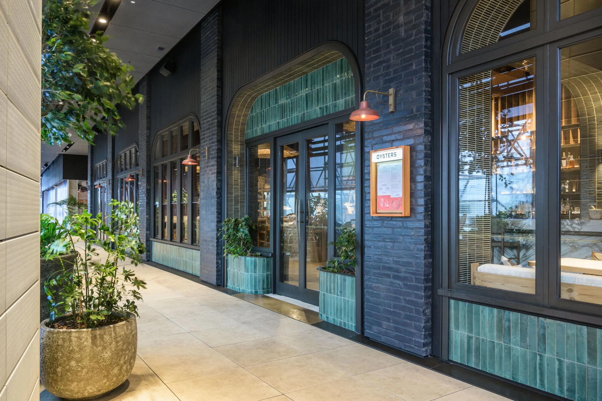 Arched dark-brick facade with green tile reveals and terracotta wall lamps