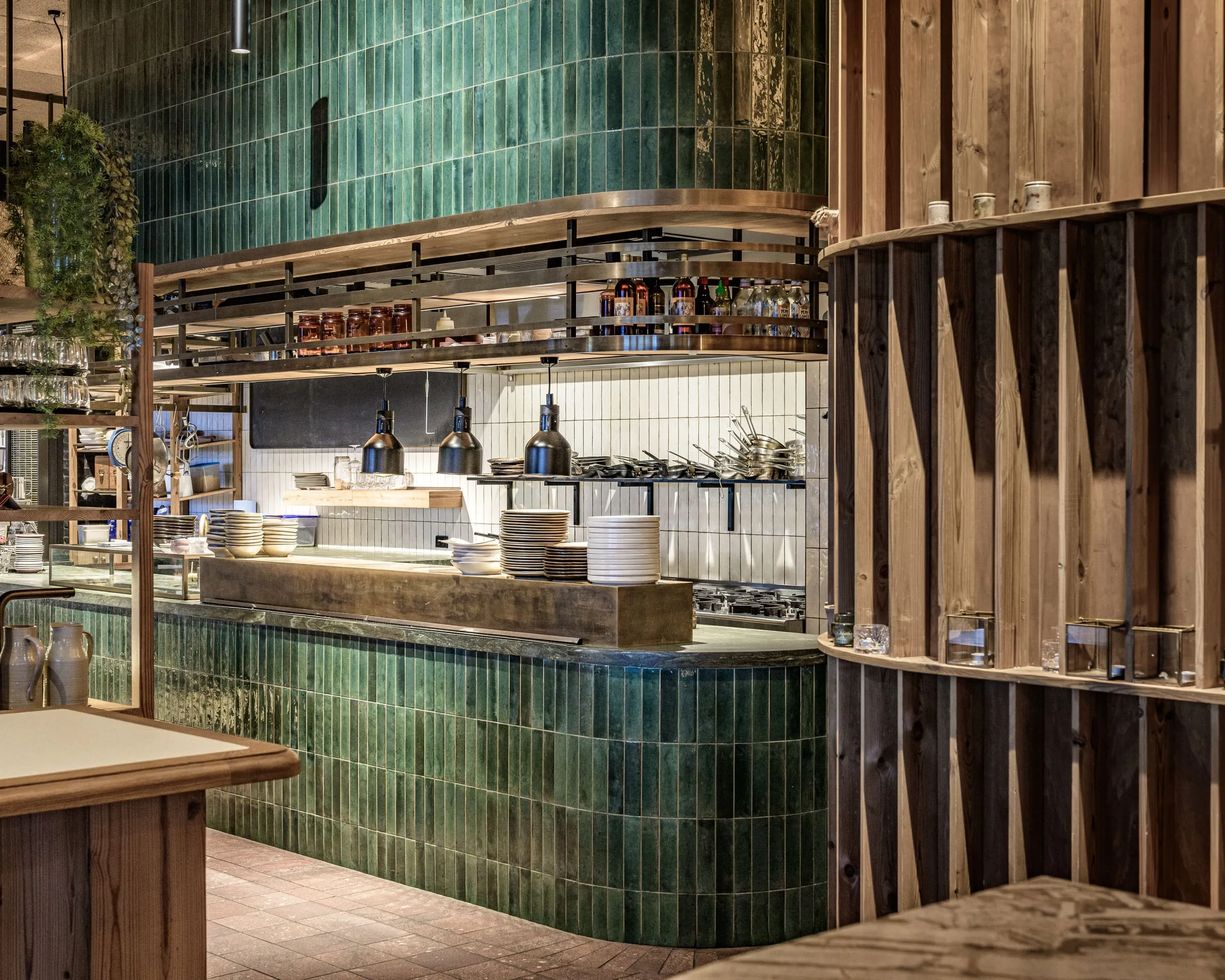 Open kitchen with green glazed tile, brass pass shelf and pine slat screens