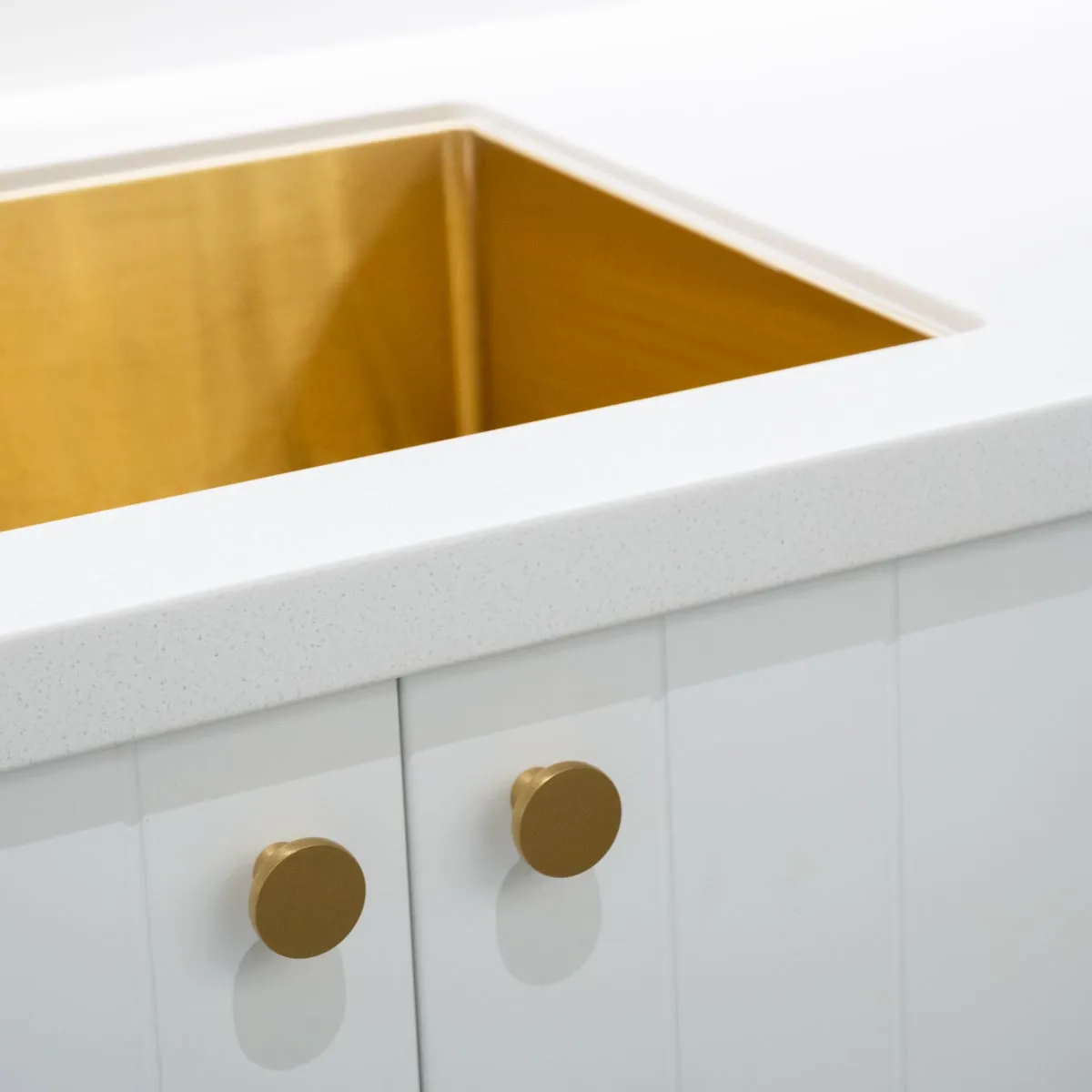 Brass undermount sink meeting the stone benchtop above V-groove doors