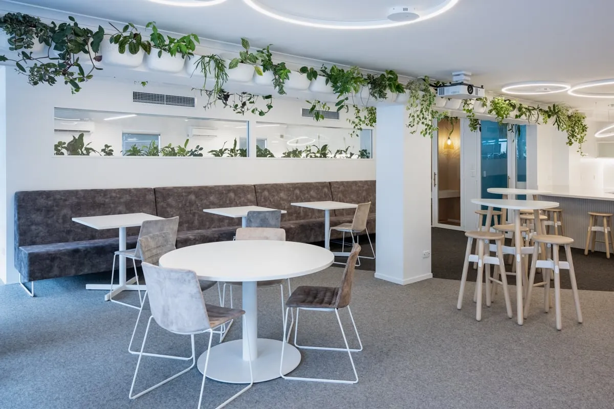 Breakout with grey banquette, planter rail greenery and café tables
