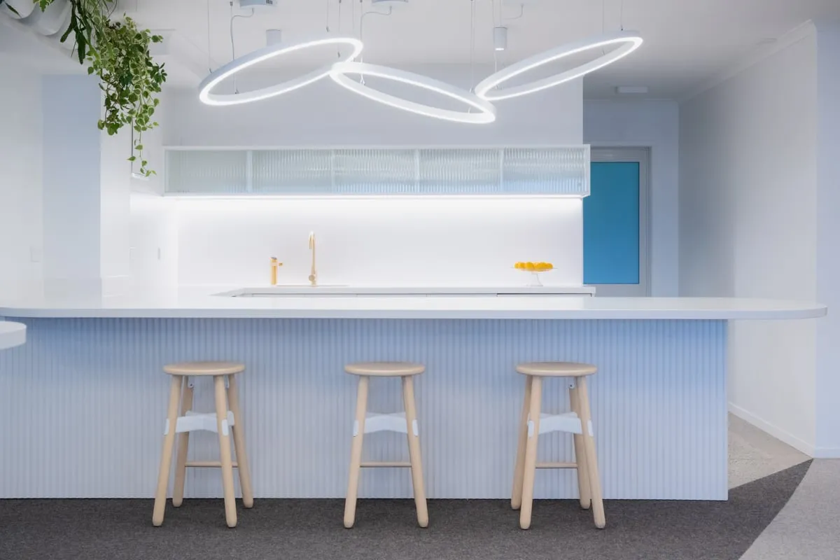 Fluted white island with three blond stools under linked ring pendants