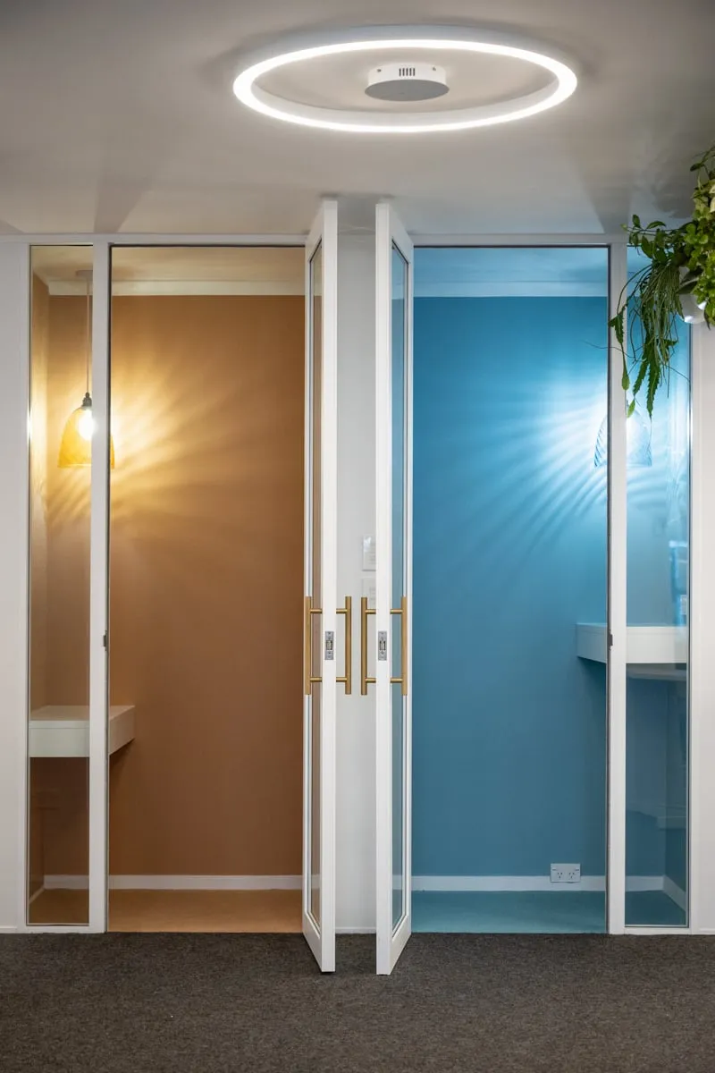 Ochre and teal phone booths glowing behind glazed doors with brass pulls