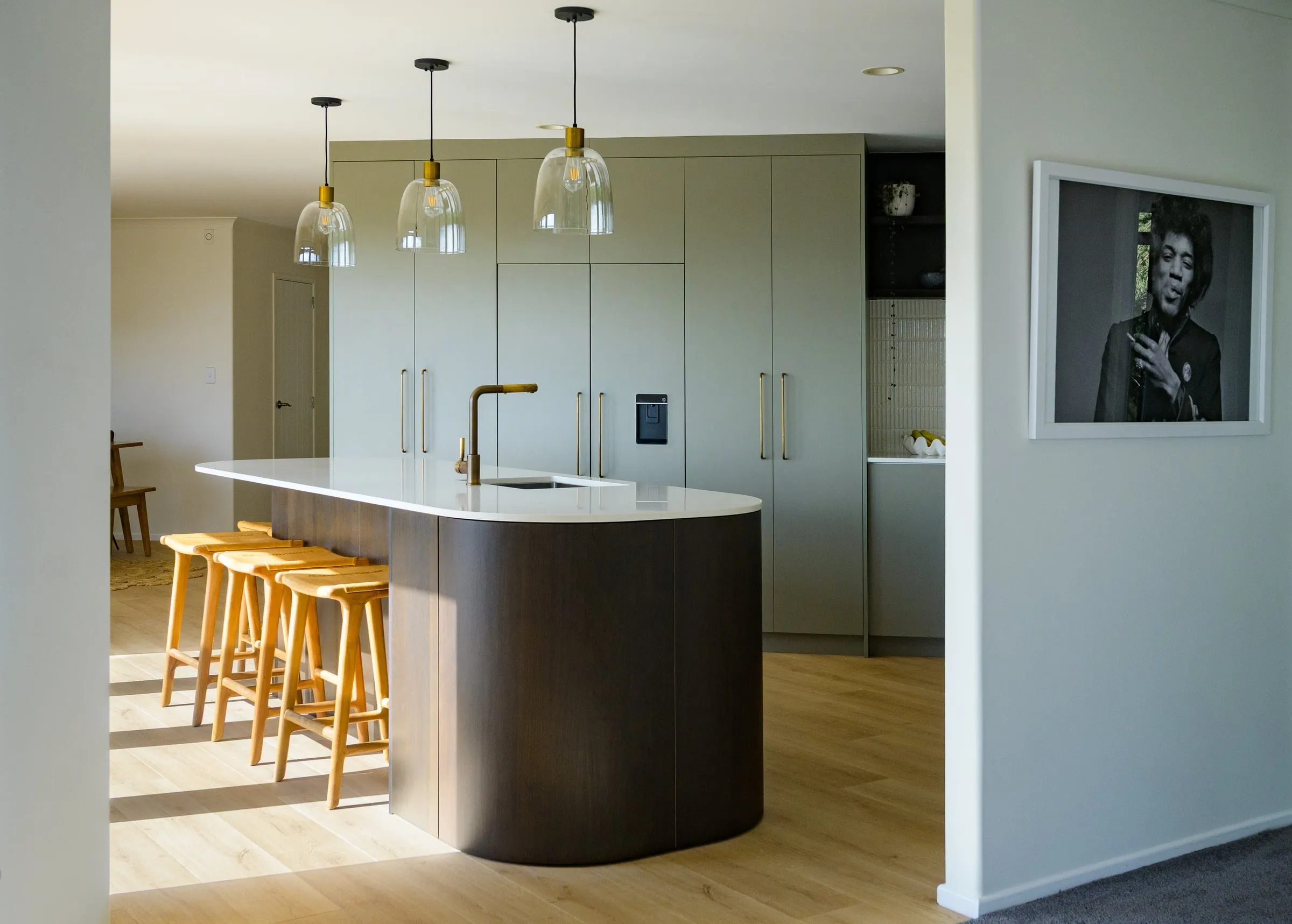 Sage kitchen with curved smoked-timber island, white stone top and brass pendants