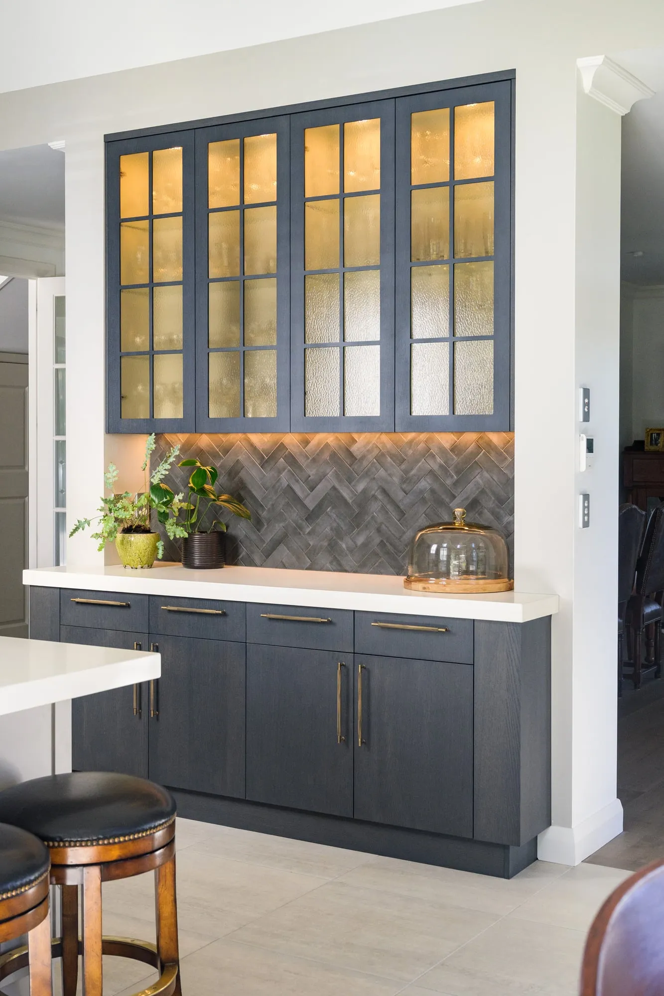 Backlit seeded-glass bar dresser with herringbone tile and brass pulls