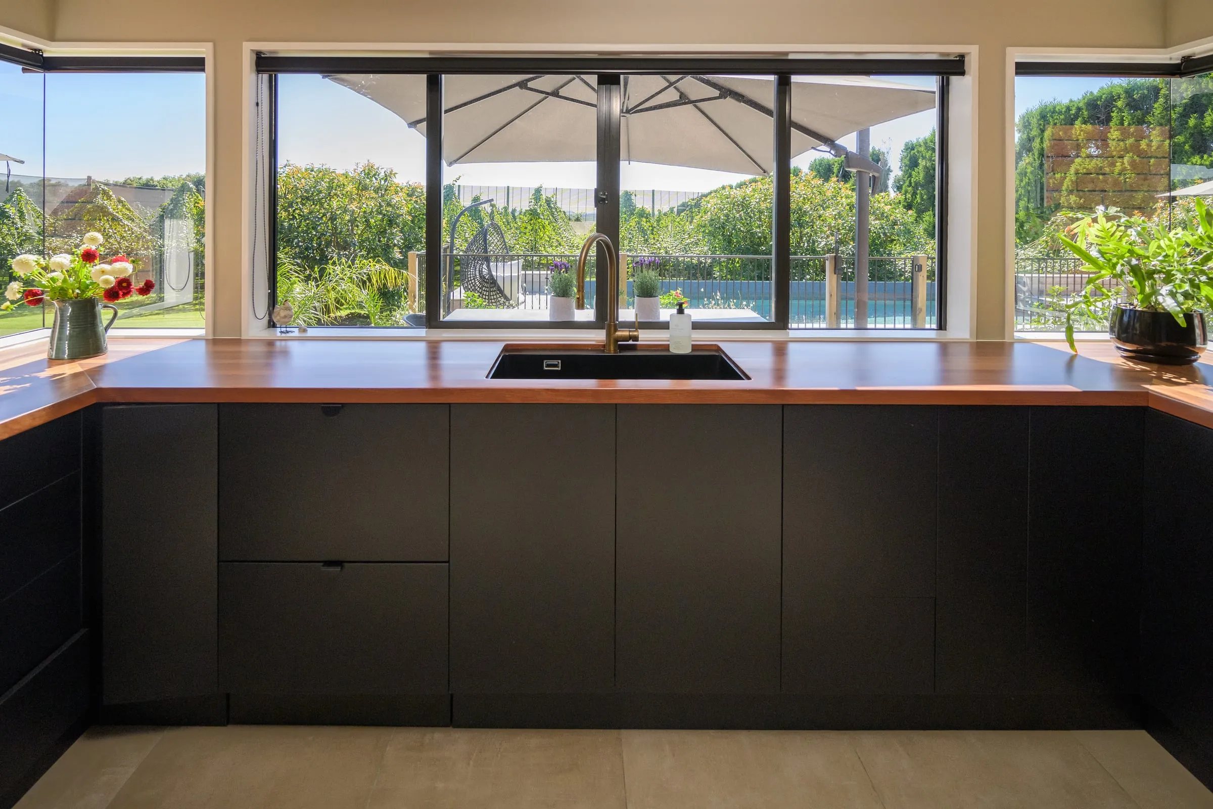 Near-symmetrical sink run with pool and orchard beyond black-framed windows