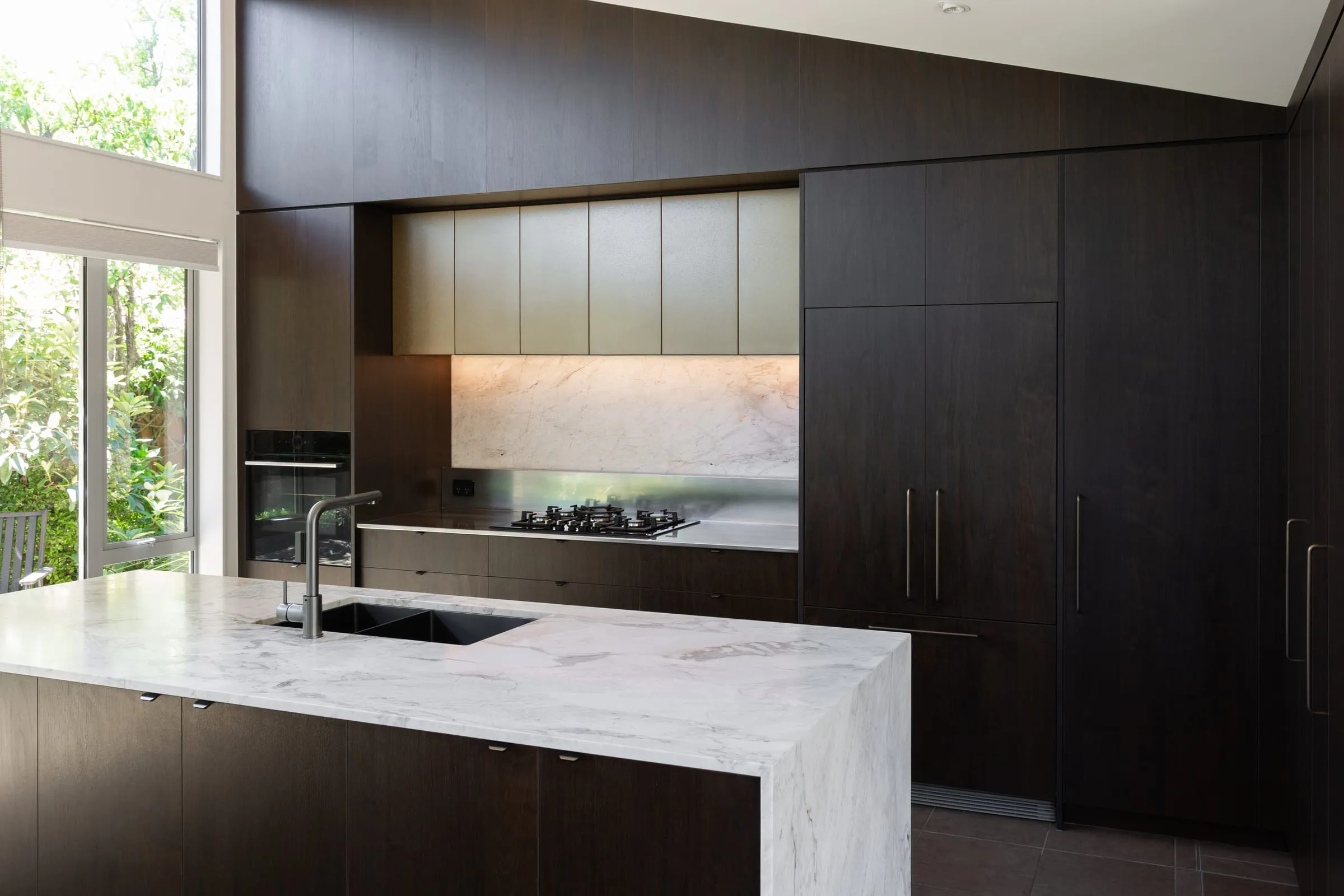 Full kitchen elevation with brass upper cabinets and glowing Quartzite splashback
