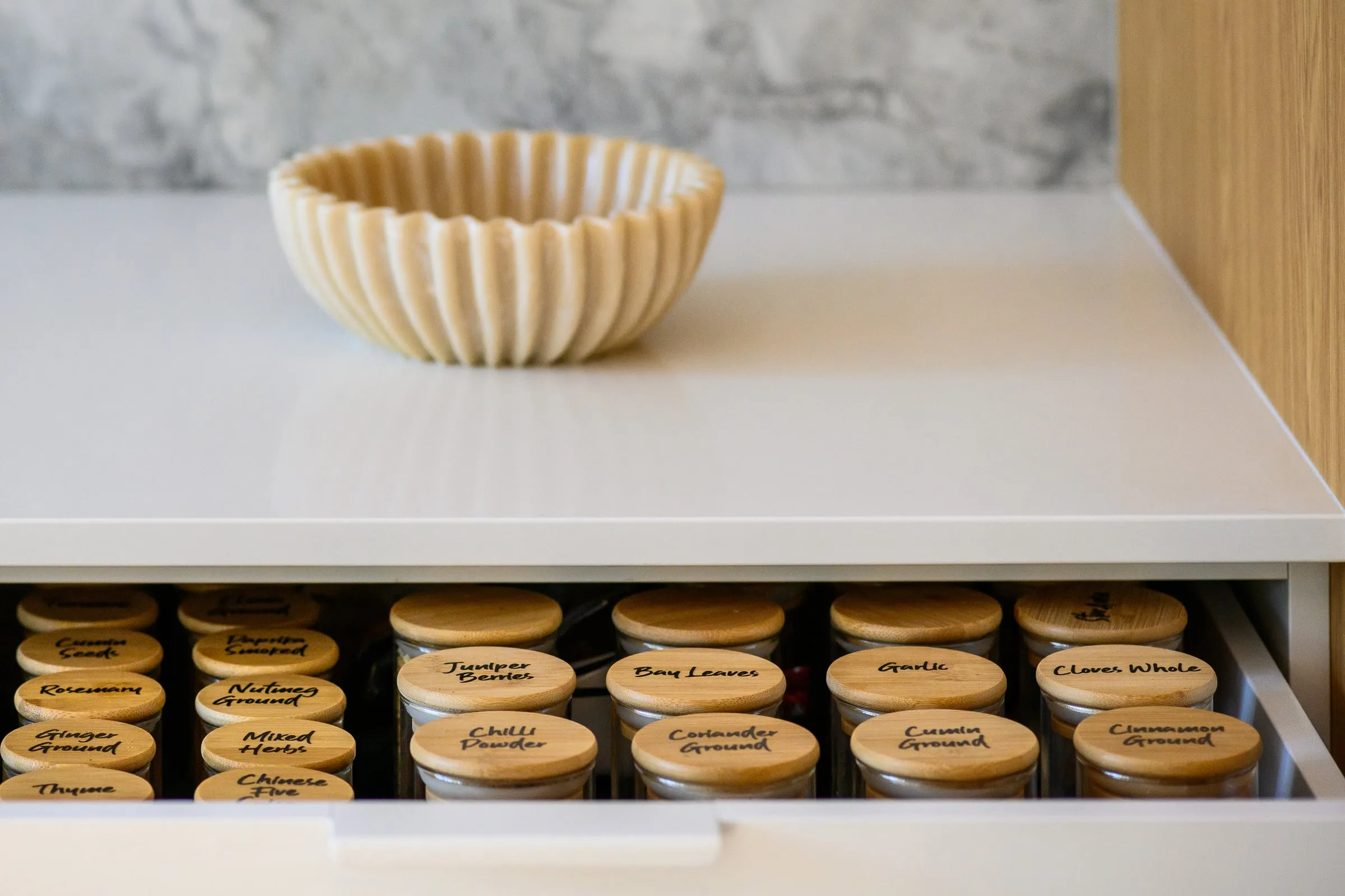 Open spice drawer with bamboo-lidded jars beneath a fluted bowl