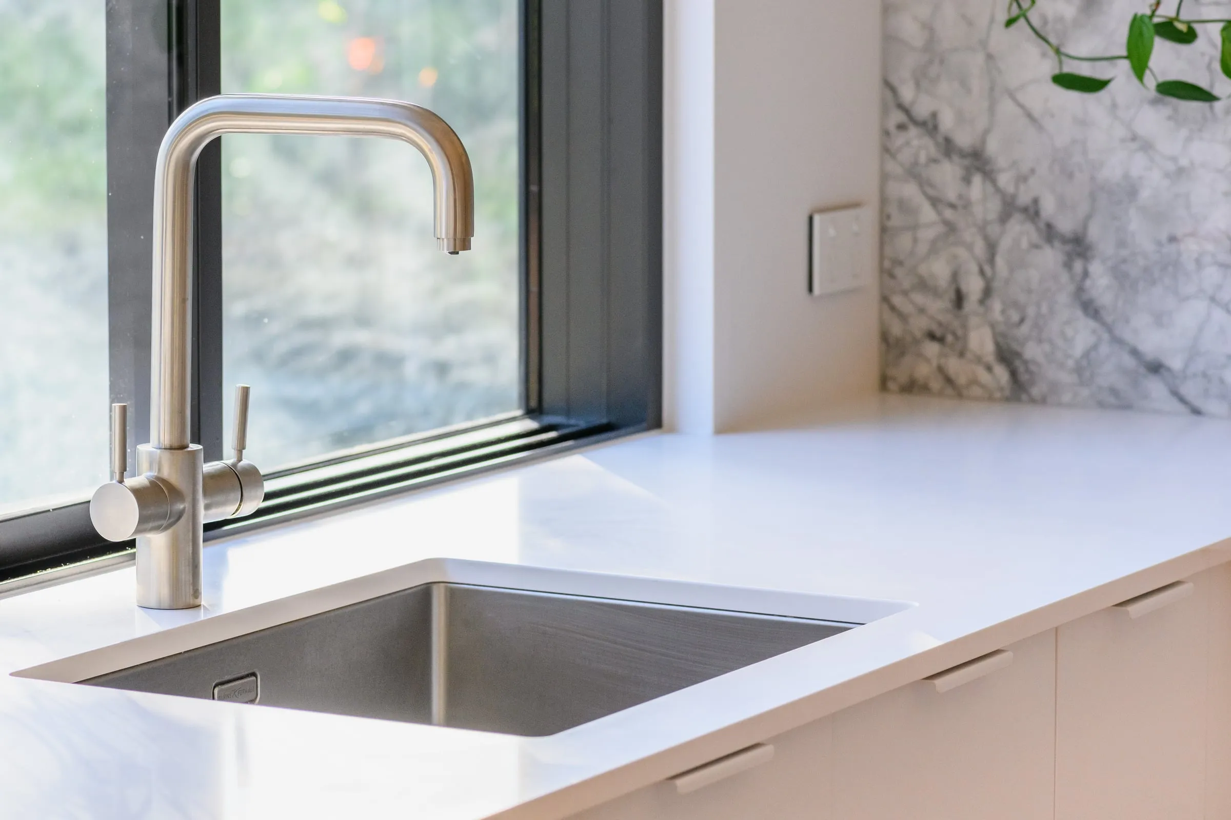 Brushed stainless tap over undermount sink against black window frame