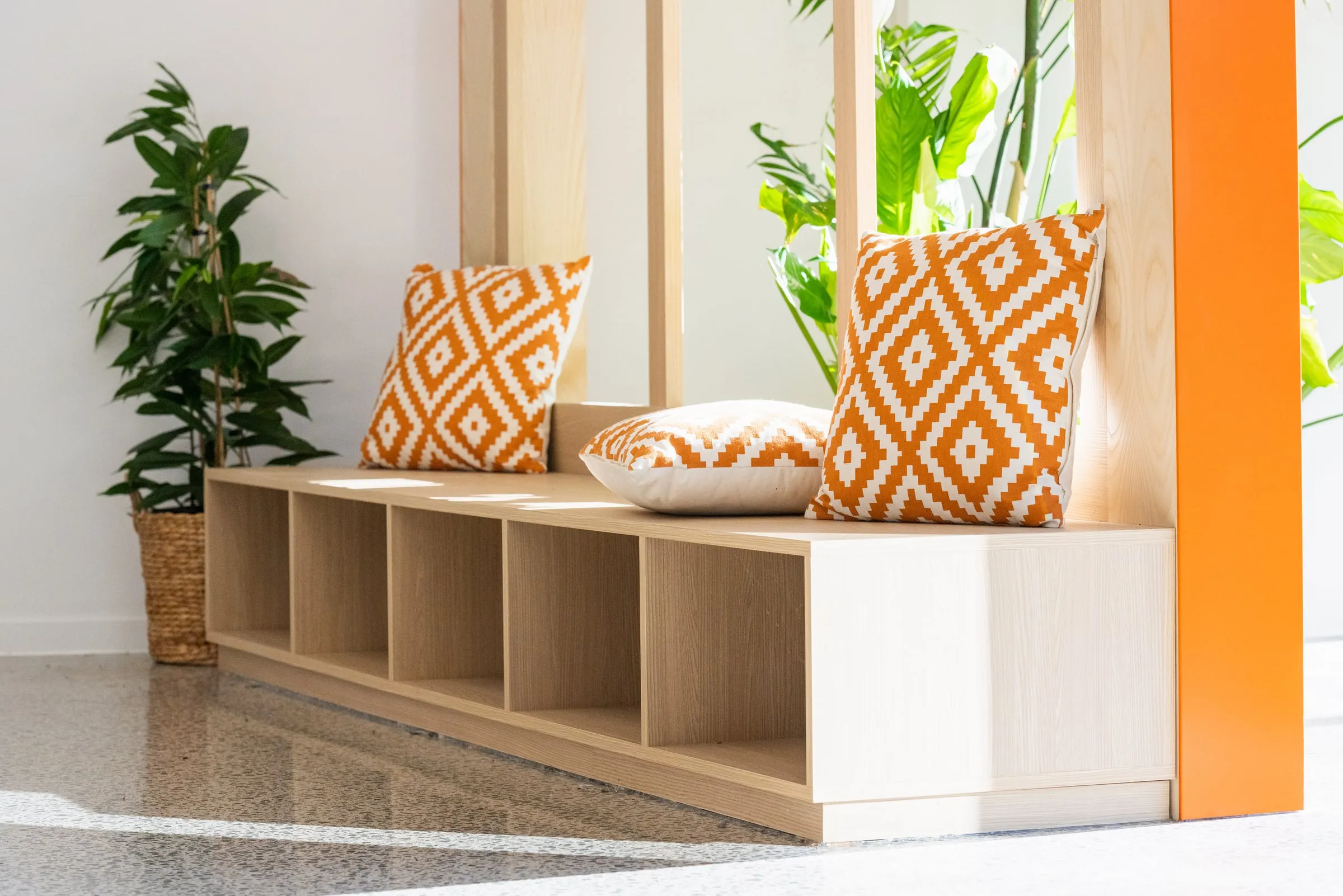 Sunlit window bench with Oak cubbies and orange geometric cushions