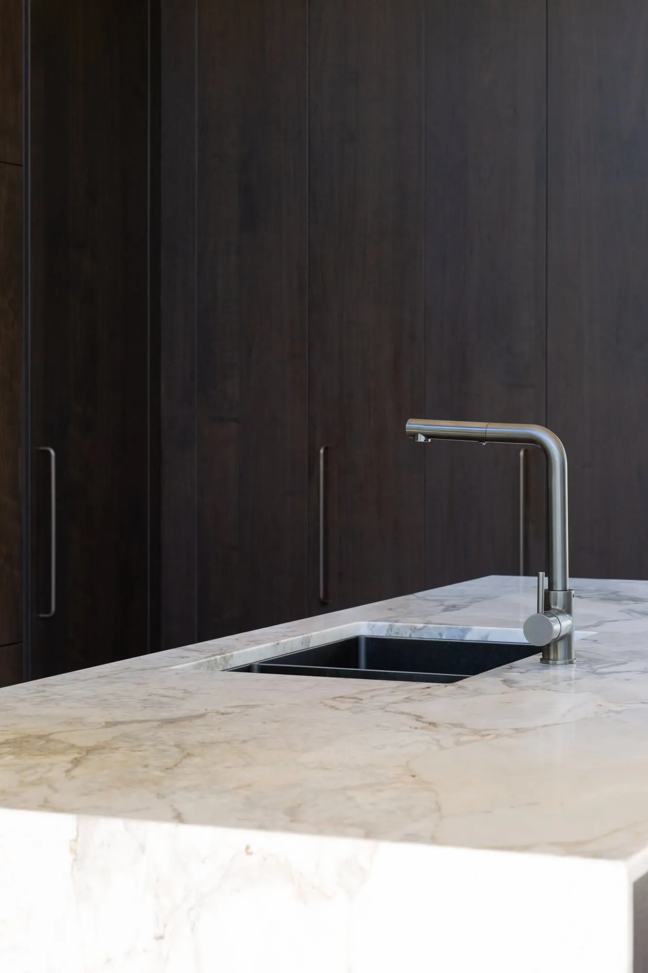 Undermount sink and brushed mixer on veined stone against dark timber