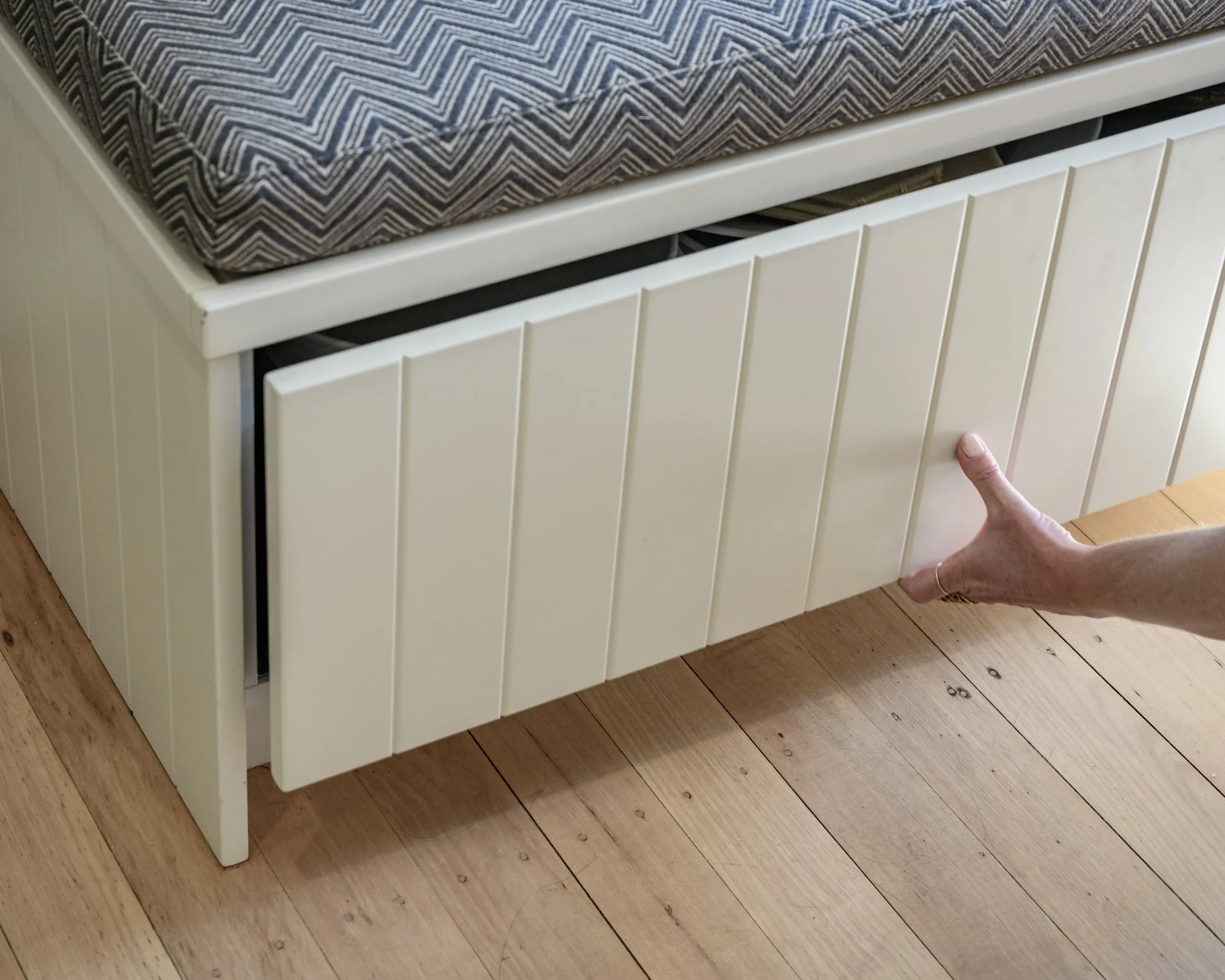 A hand drawing open the full-width storage drawer beneath the window seat