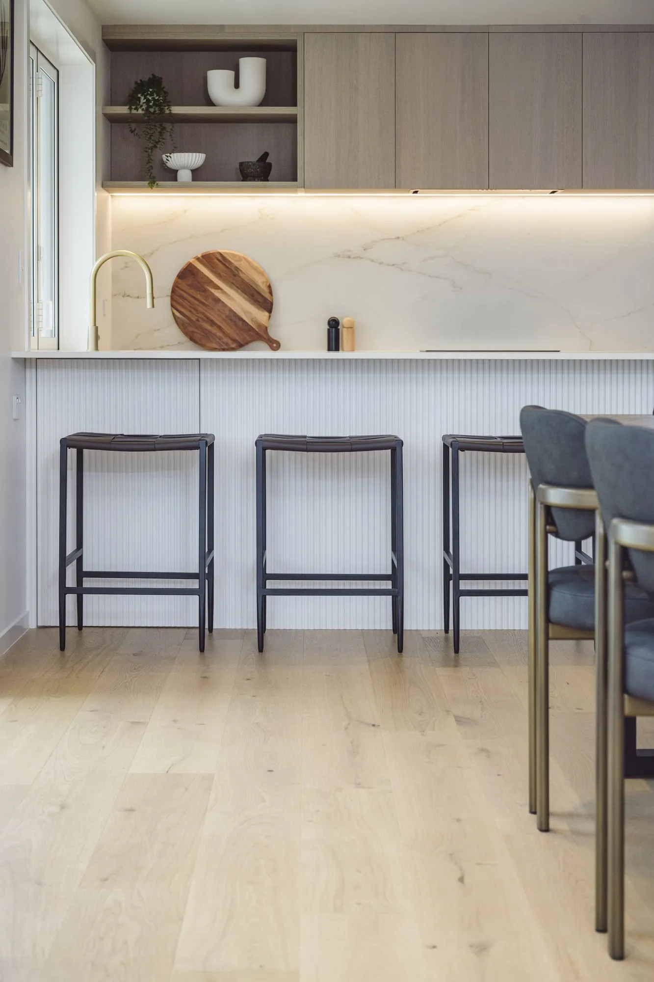 Three woven-leather stools against the fluted island under warm strip light